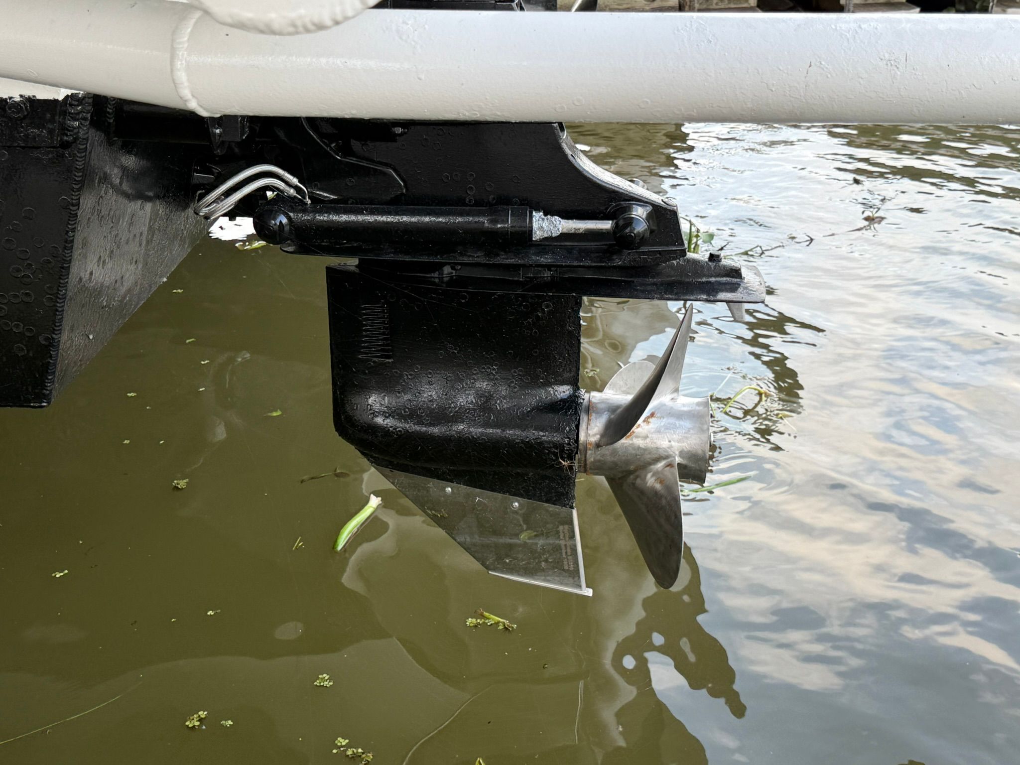 A boat motor with a propeller in the water, partially obscured by a white hull.