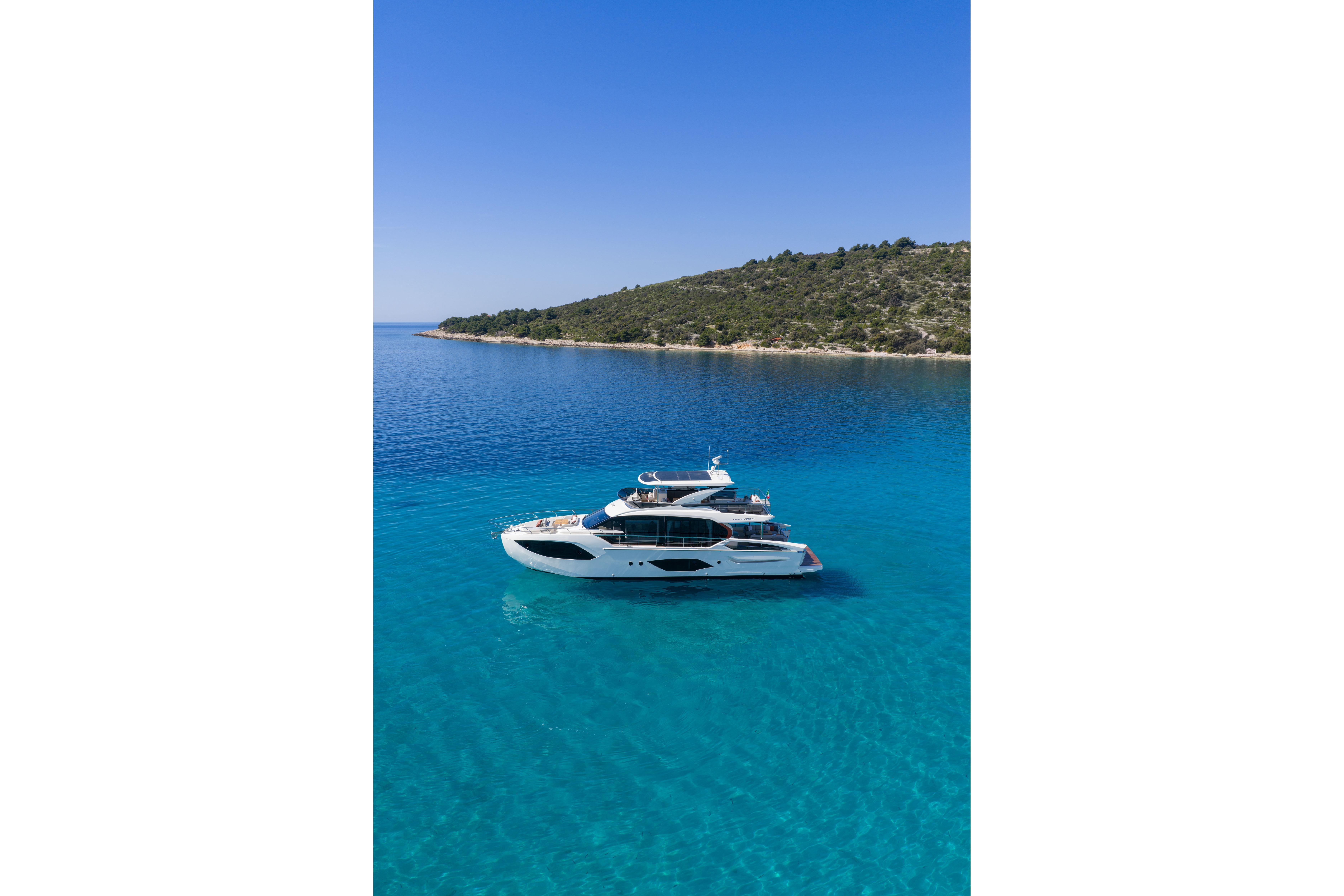 Luxury yacht on clear blue water near a wooded coastline.