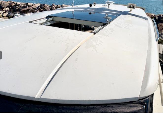 2016 Carver C37 yacht roof with open sunroof, docked by rocky shoreline.