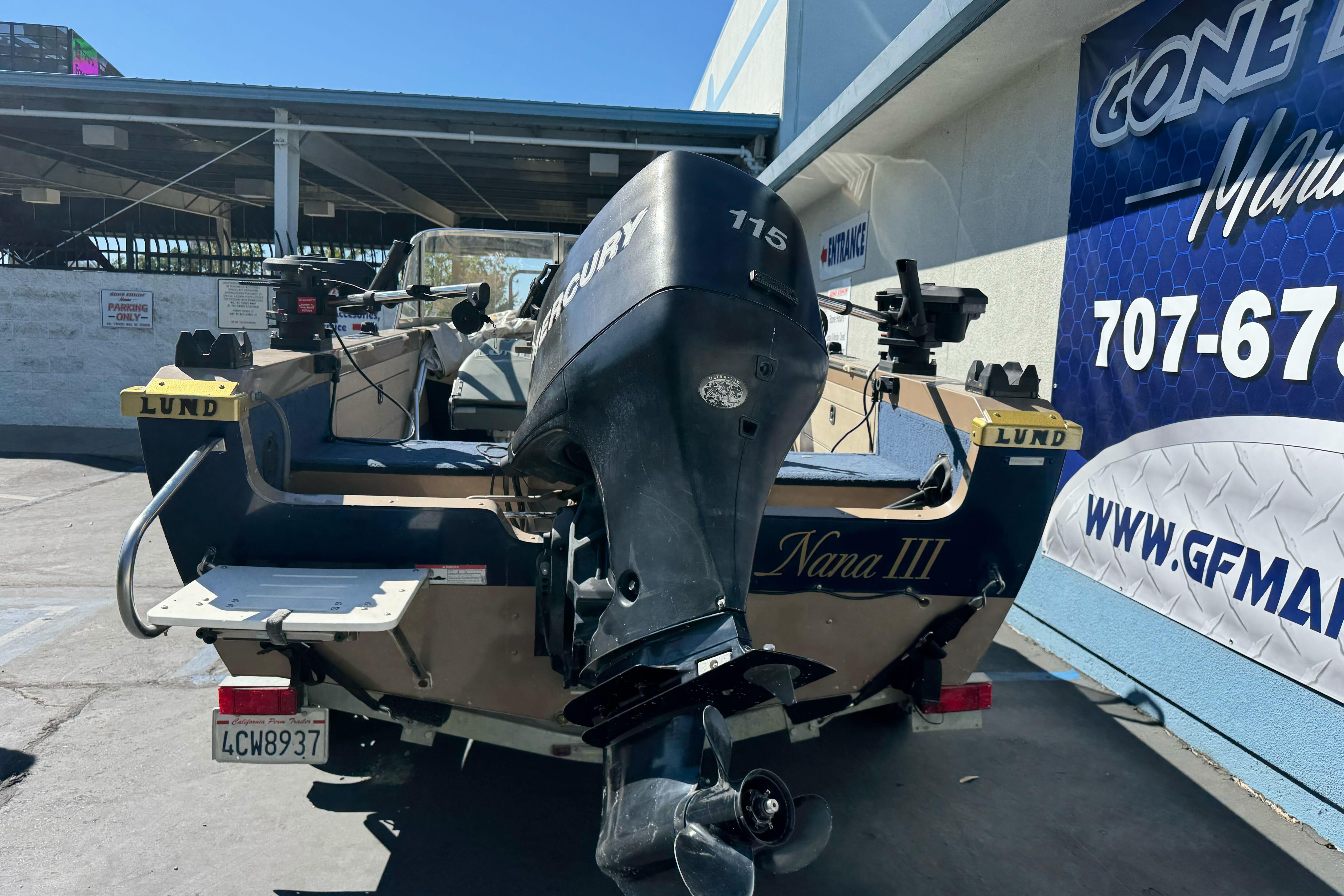 1998 Lund 1700 Pro Sport boat with Mercury engine, parked outside a marine shop.