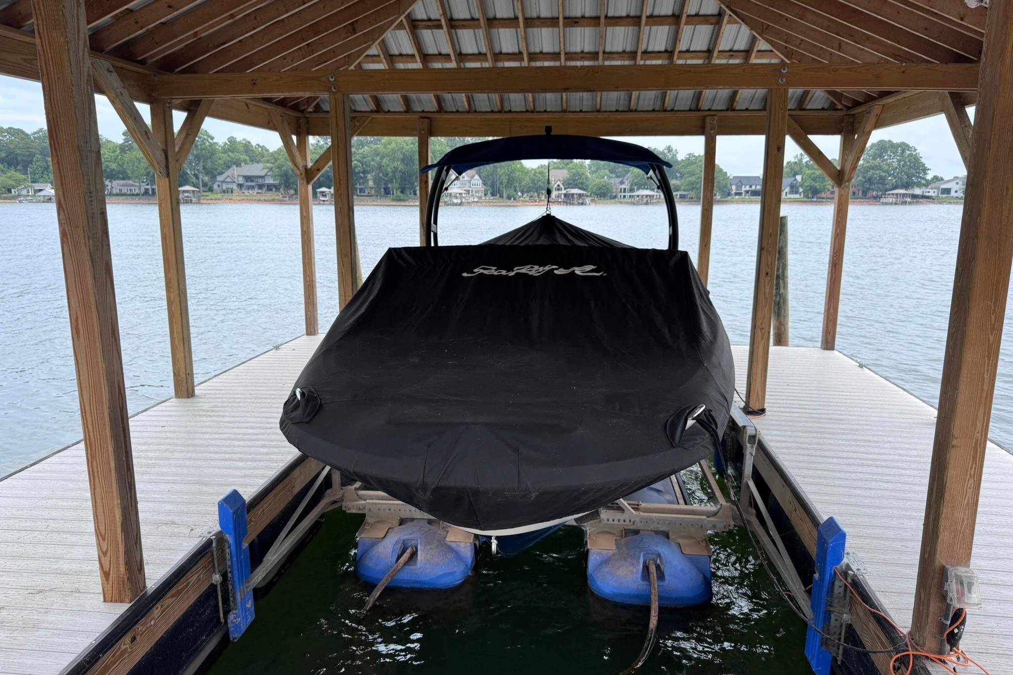 Covered 2021 Sea Ray SPX 230 boat docked under wooden shelter by the lake.