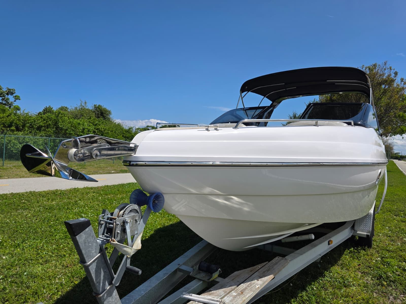 A white boat on a trailer with a black canopy, set against a blue sky background.