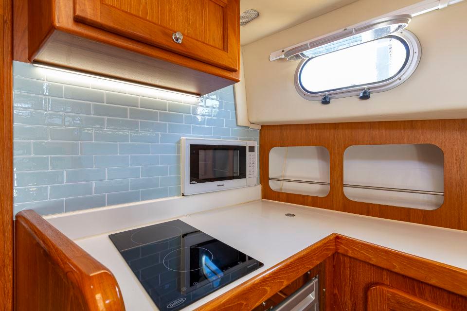 Compact kitchen in a 2002 Hardy Commodore 42 yacht with stove, microwave, and wooden cabinetry.