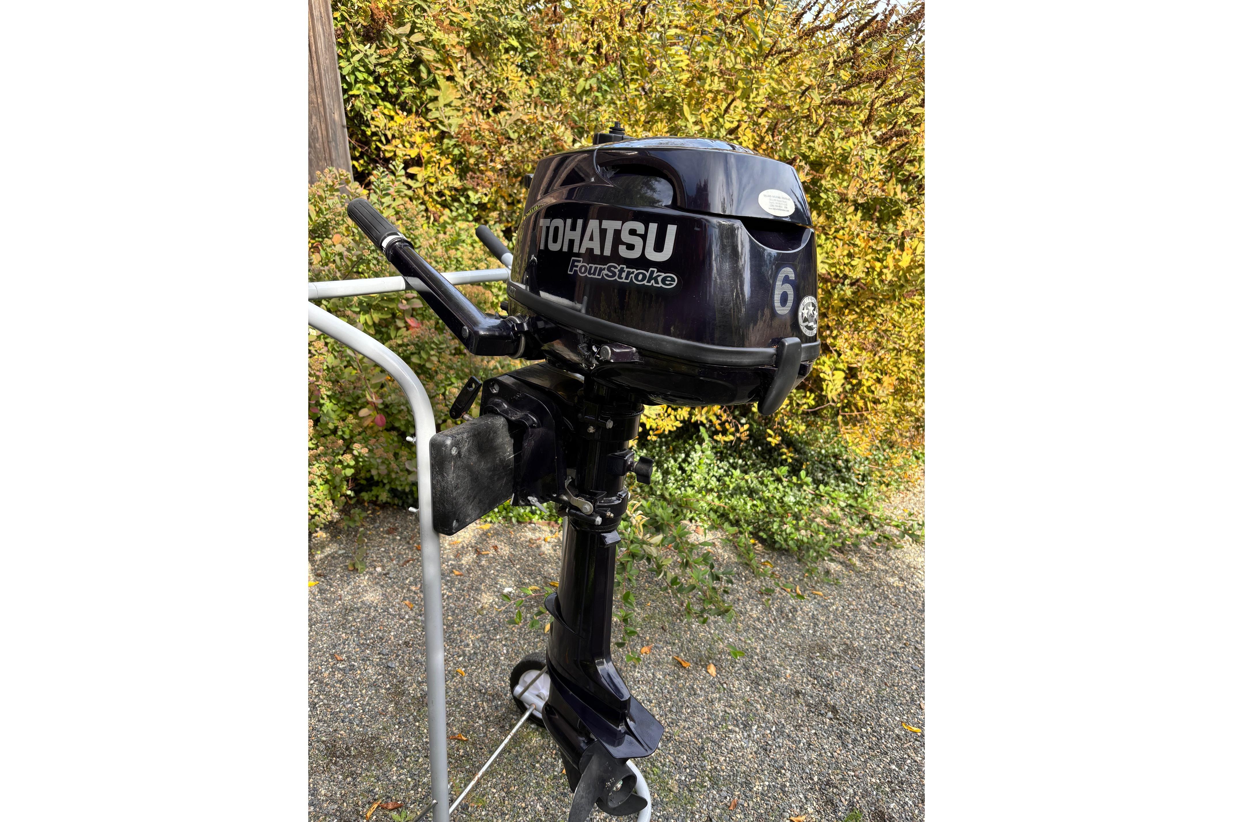 Tohatsu 6HP Four-Stroke outboard motor on a stand, outdoors with foliage background.