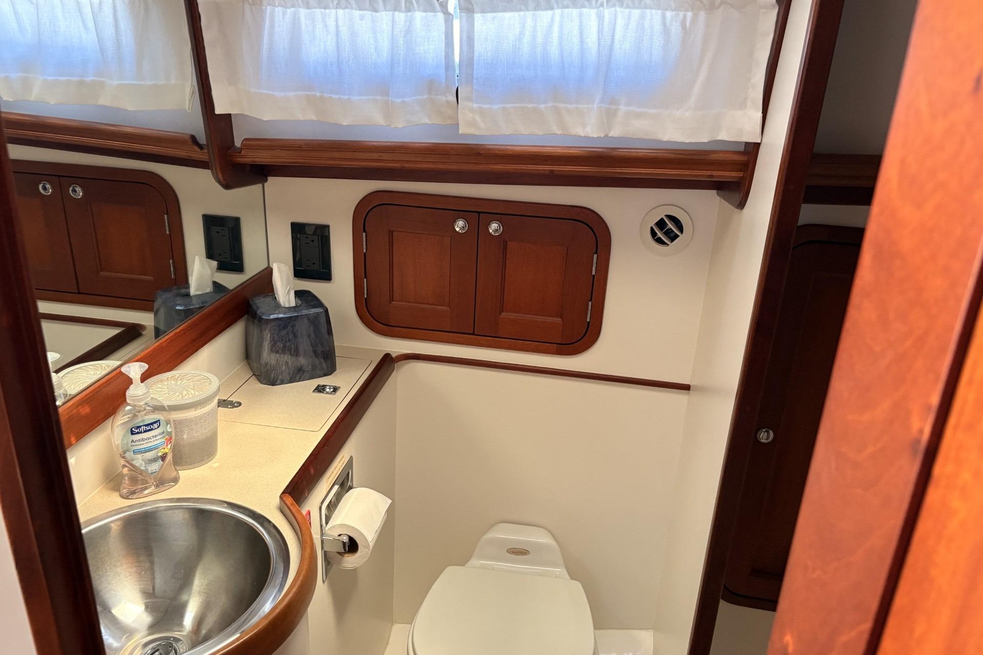 Compact bathroom with wooden cabinets, stainless steel sink, and white curtains.