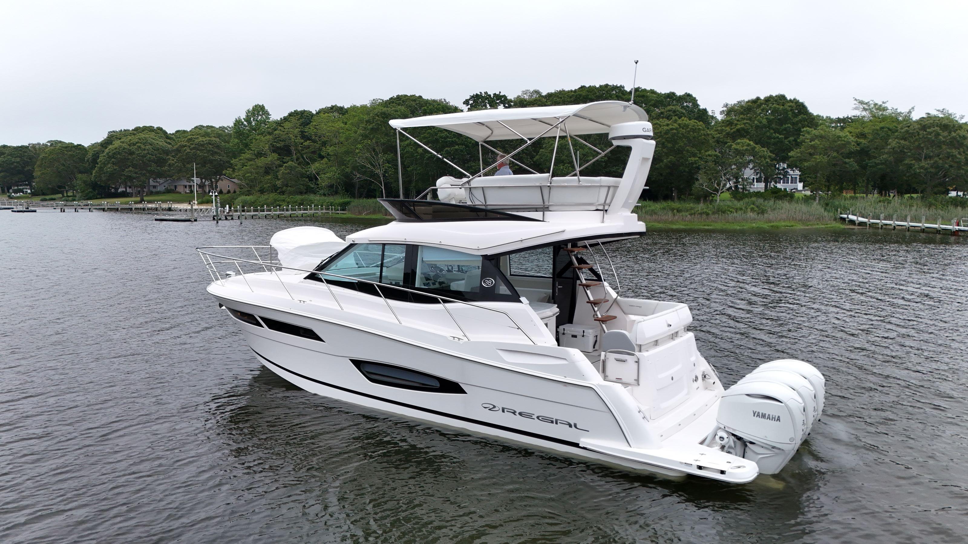 2025 Regal 38 FXO yacht on a serene lake with lush green shoreline.