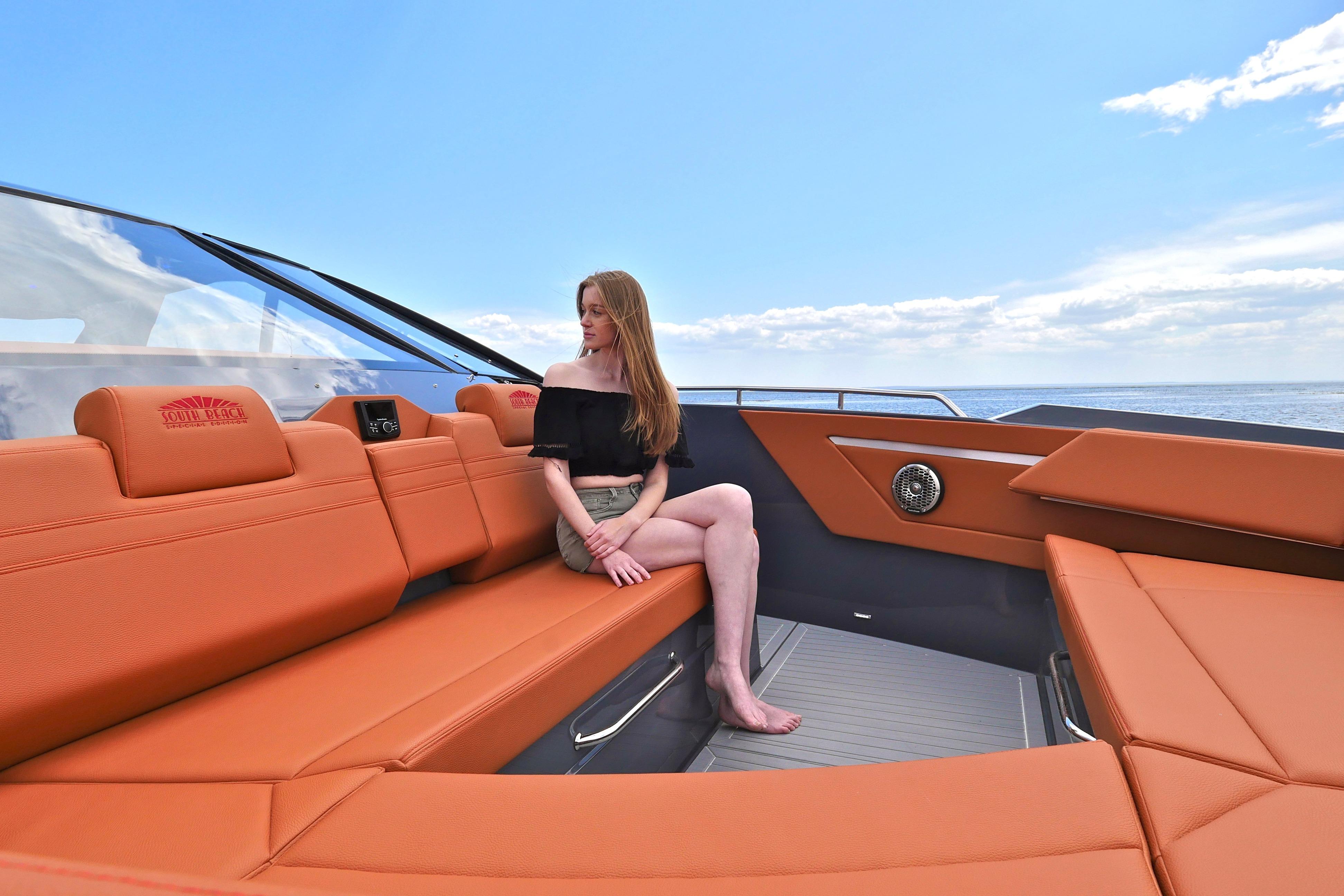 Woman relaxing on 2026 Cruisers Yachts 42 GLS I/O with orange seating, ocean view.