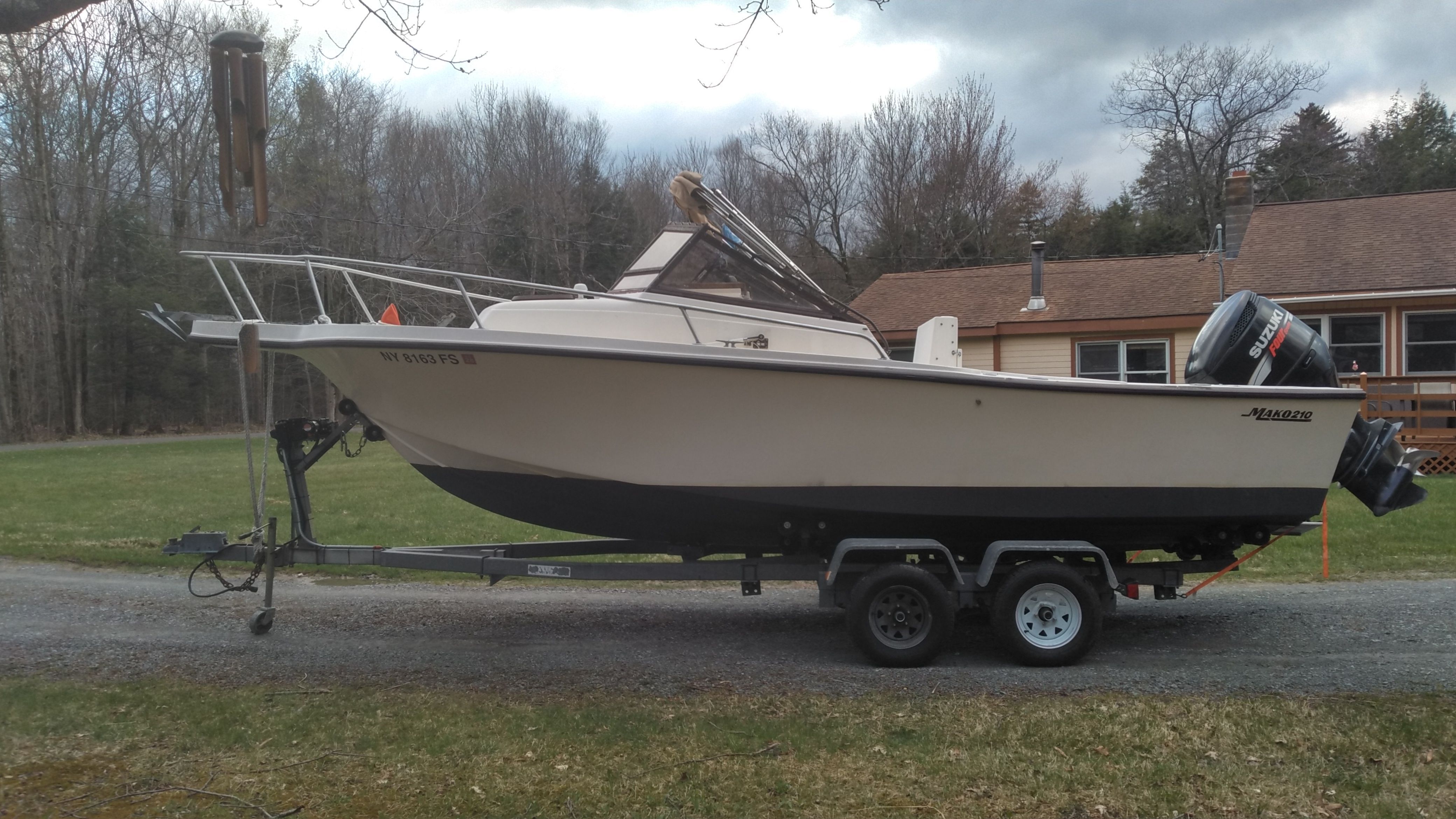 A Mako 240 walk around boat on a trailer, parked on a gravel path in front of a house.
