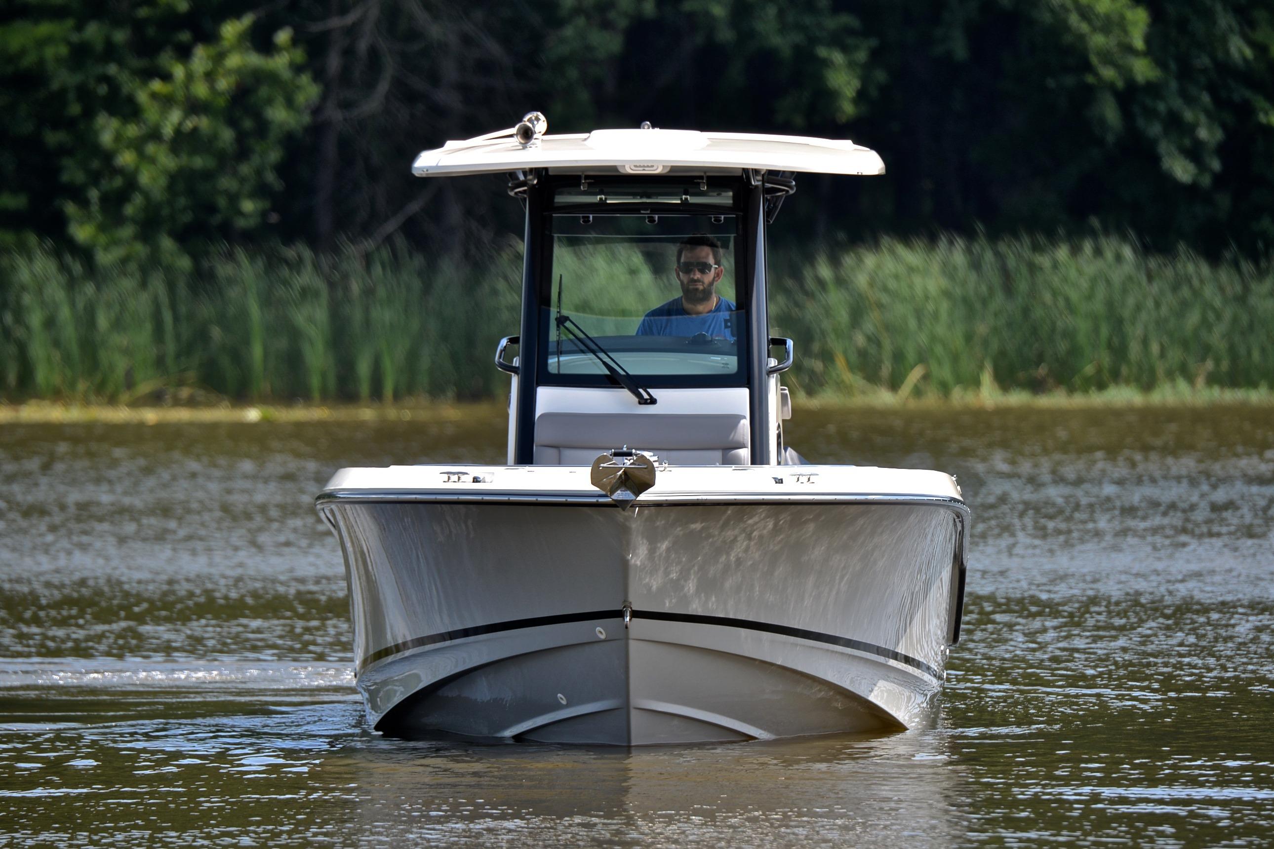2024 Boston Whaler 250 Outrage boat cruising on a calm lake with lush greenery.