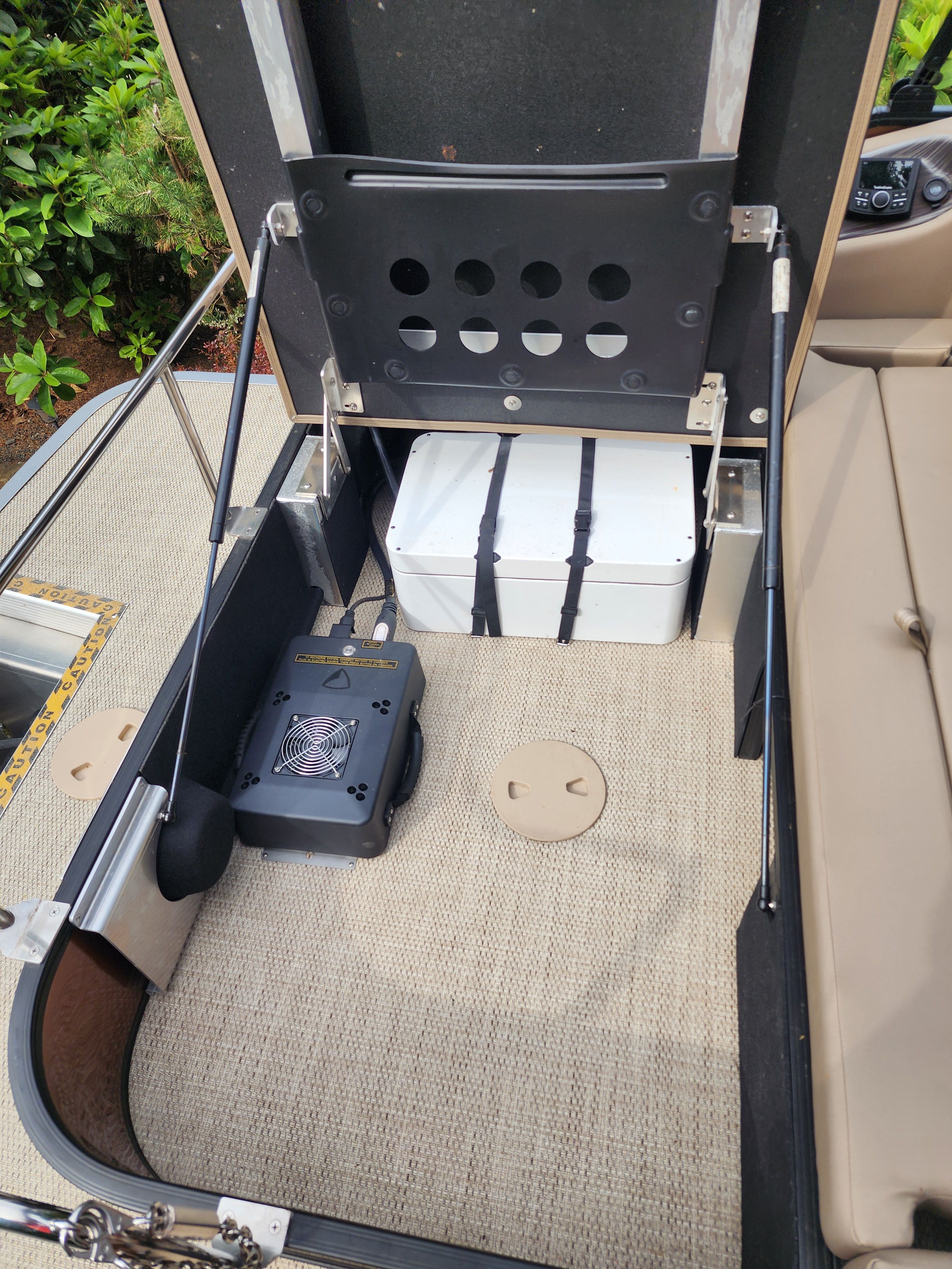 An open storage compartment on a boat with a white container and an electrical device.