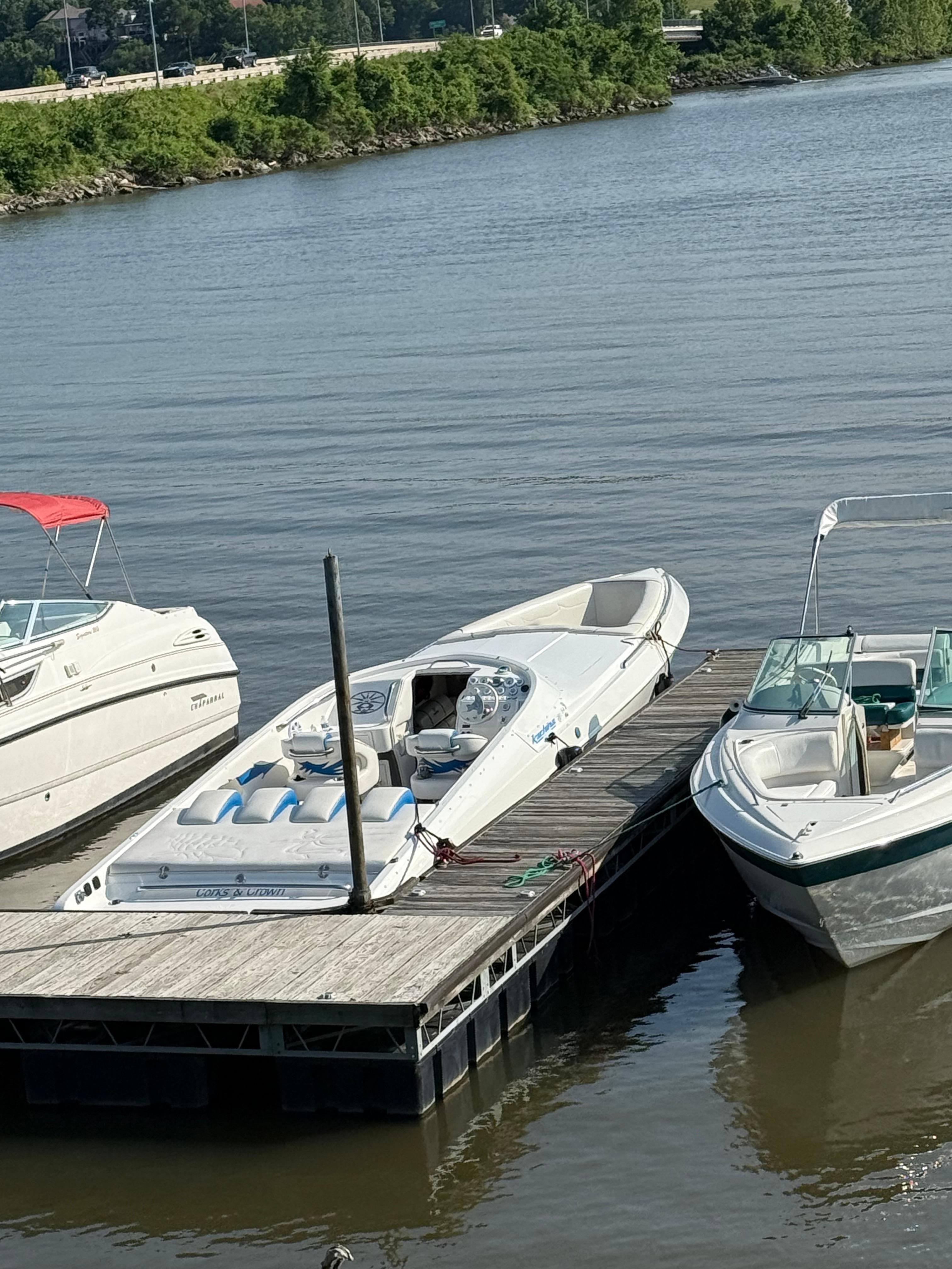 2005 Kachina Bolero boat docked between two other boats on a calm river.