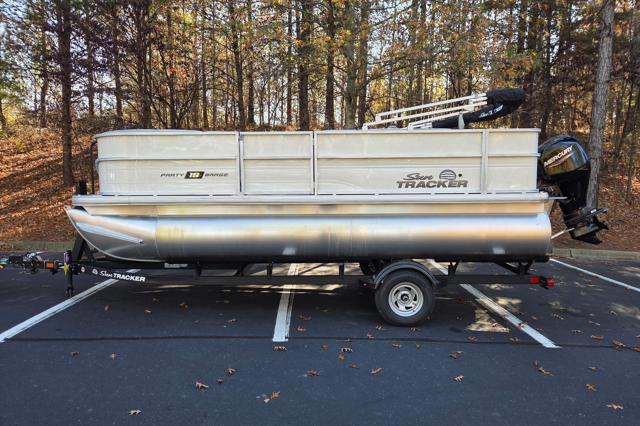 2026 Sun Tracker Party Barge 18 DLX pontoon boat in a wooded parking area.