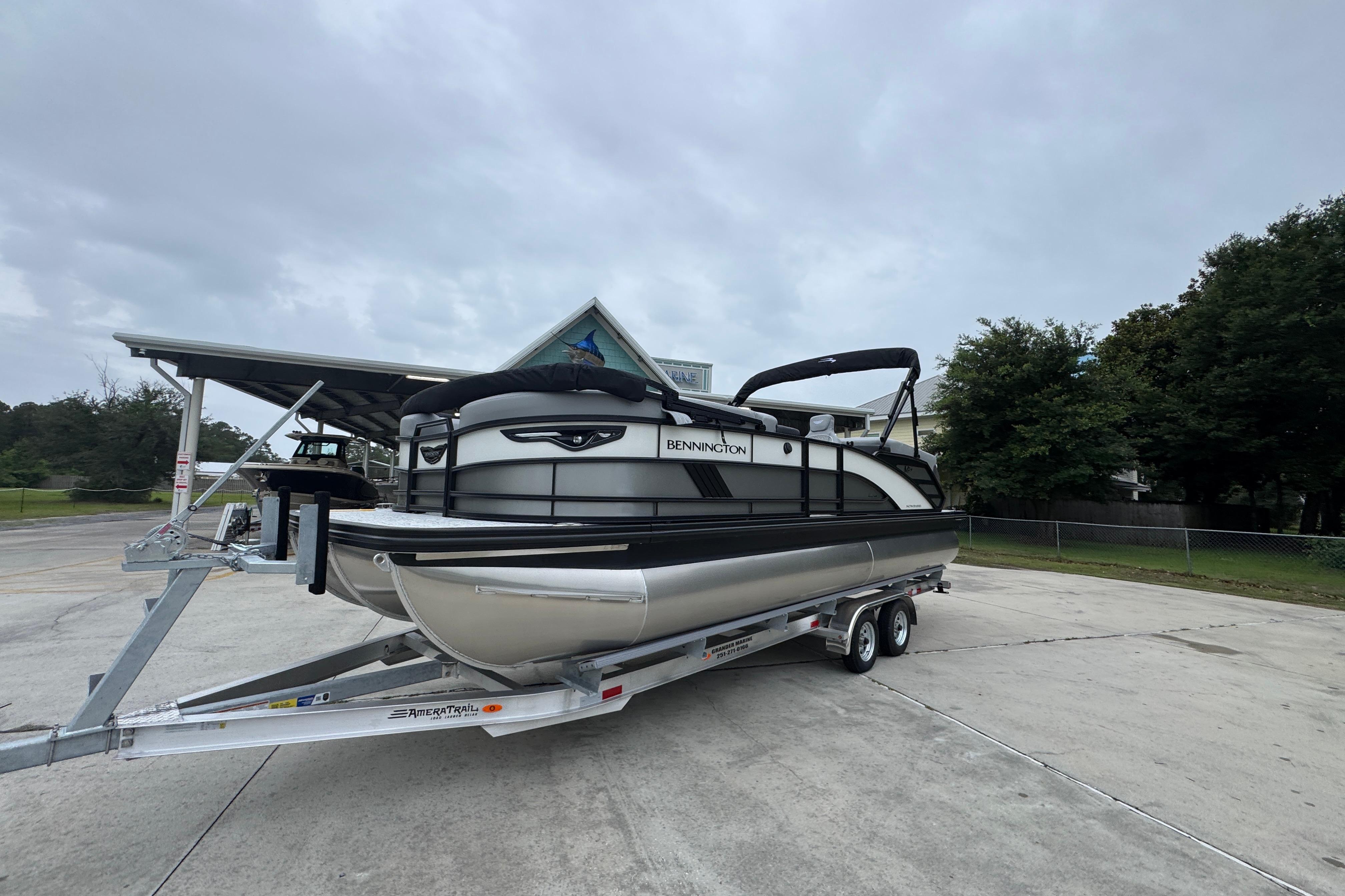 2027 Bennington 24 MFB pontoon boat on trailer, parked outdoors under cloudy sky.