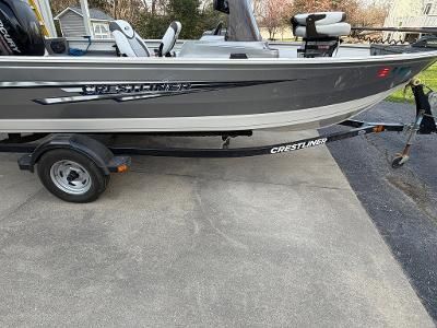A gray Crestliner boat on a trailer, parked on a driveway.