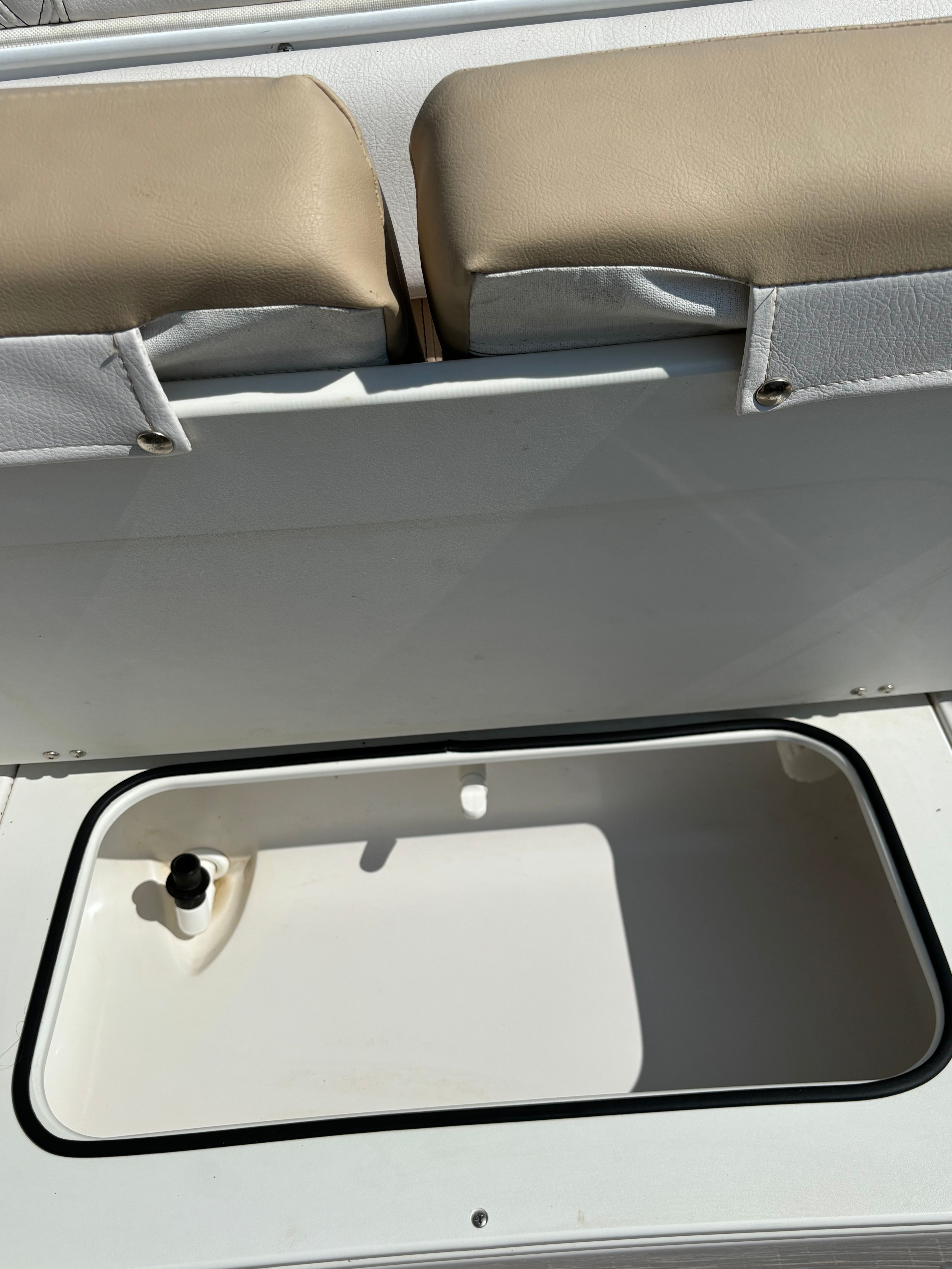 An open storage compartment on a boat with beige cushions.