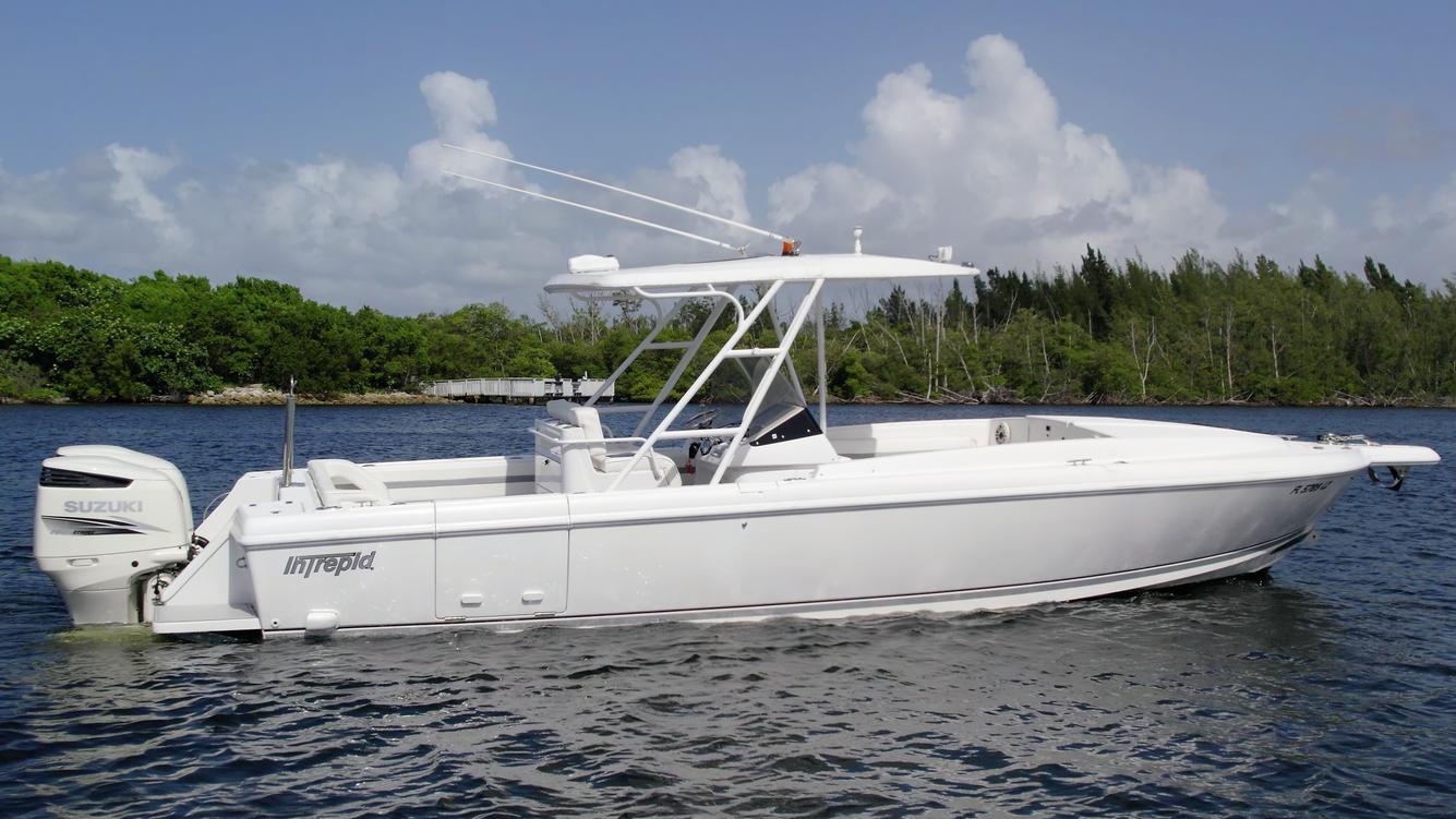 2003 Intrepid 32 boat on water, white hull, outboard motor, clear sky, lush greenery background.