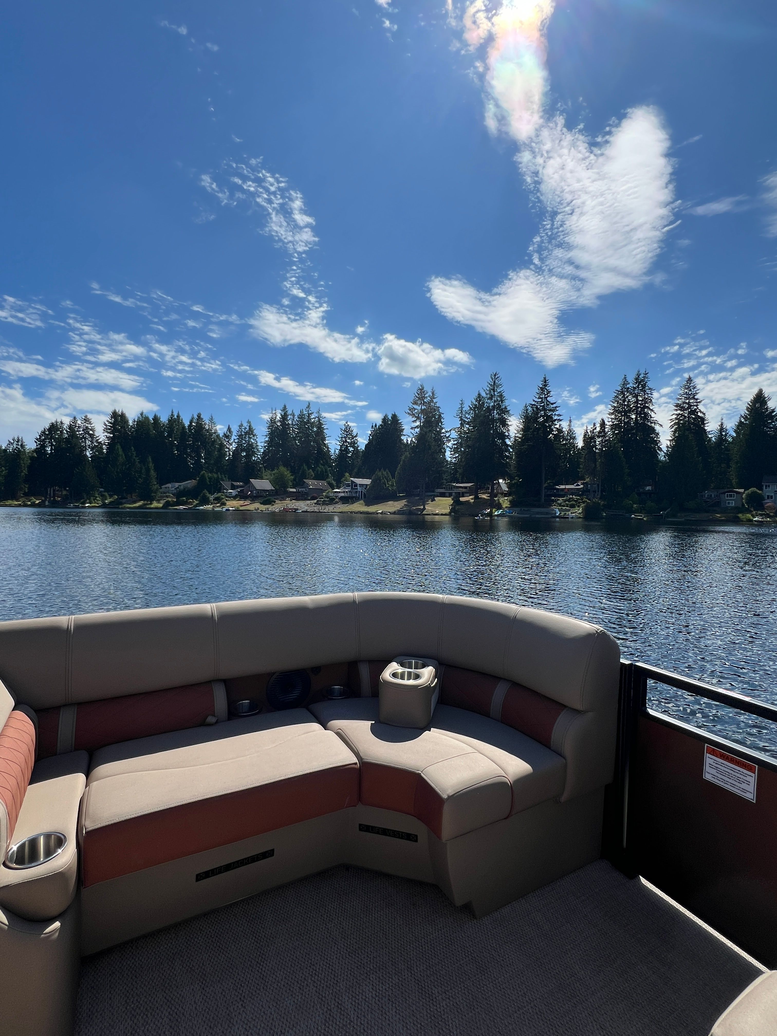 A Bennington 22 LSB pontoon boat with beige seating on a calm lake under a blue sky.