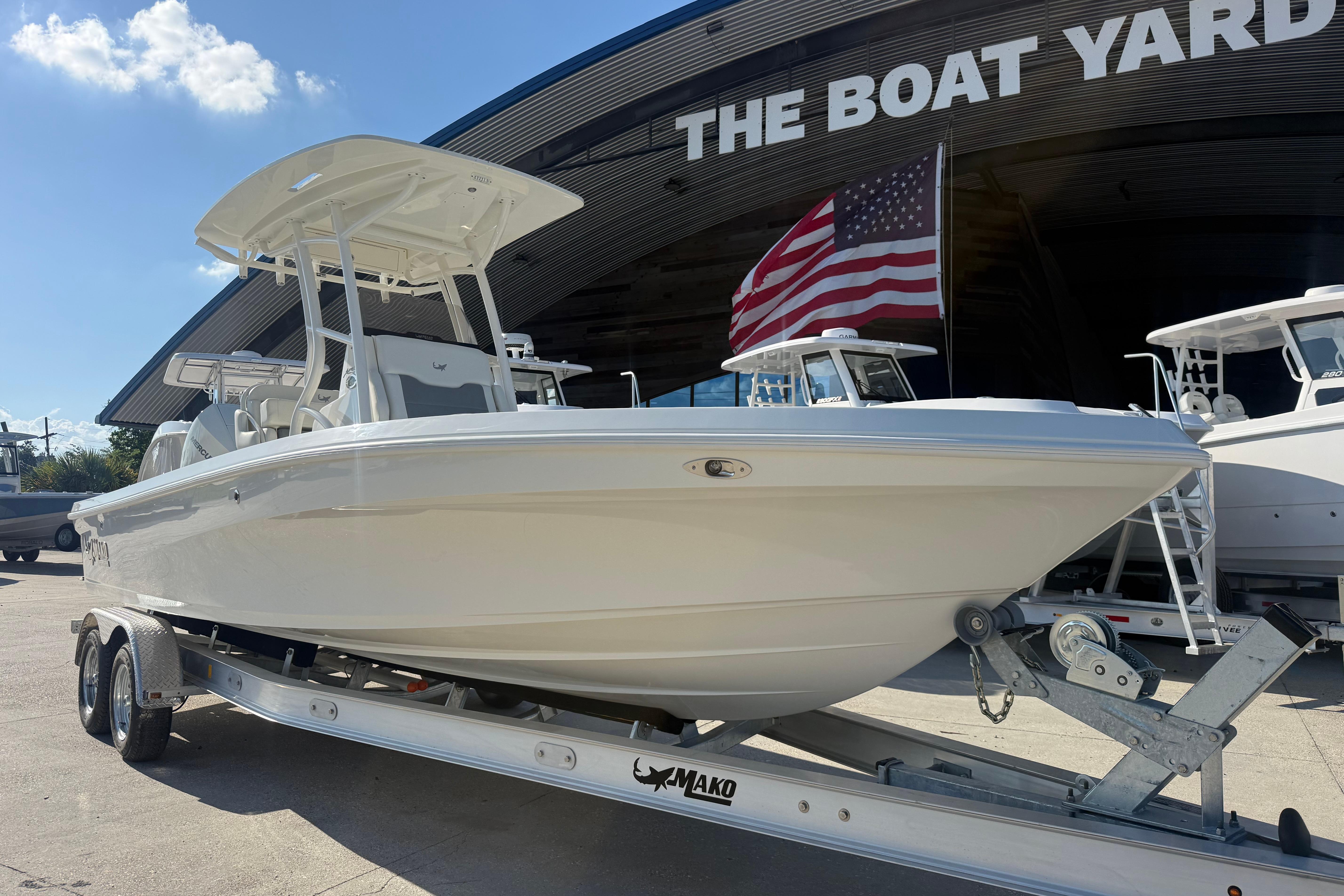 2026 Mako 24 APEX boat on trailer at dealership, American flag in background.