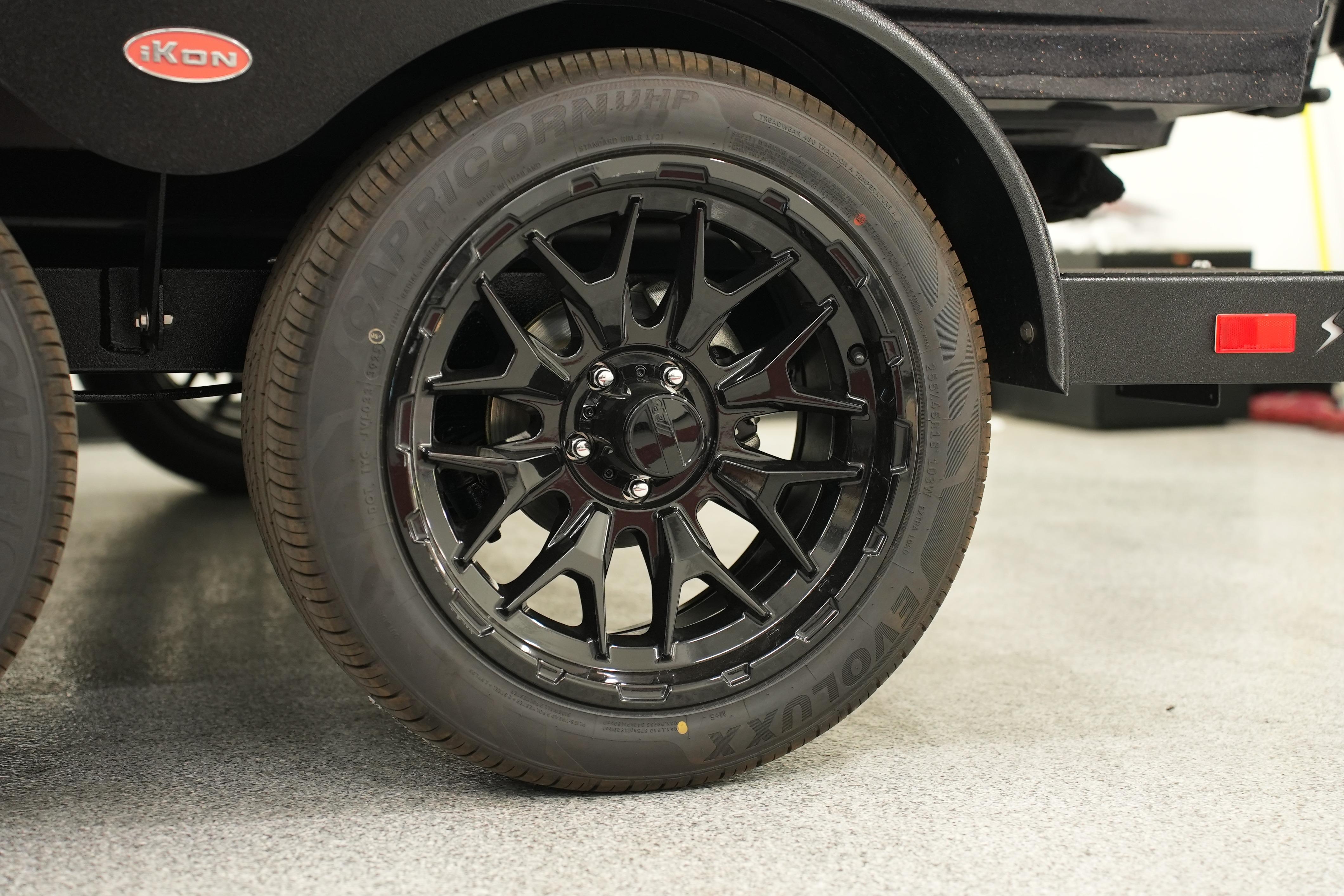 Black alloy wheel of 2026 iKon LXE20 vehicle on a showroom floor.