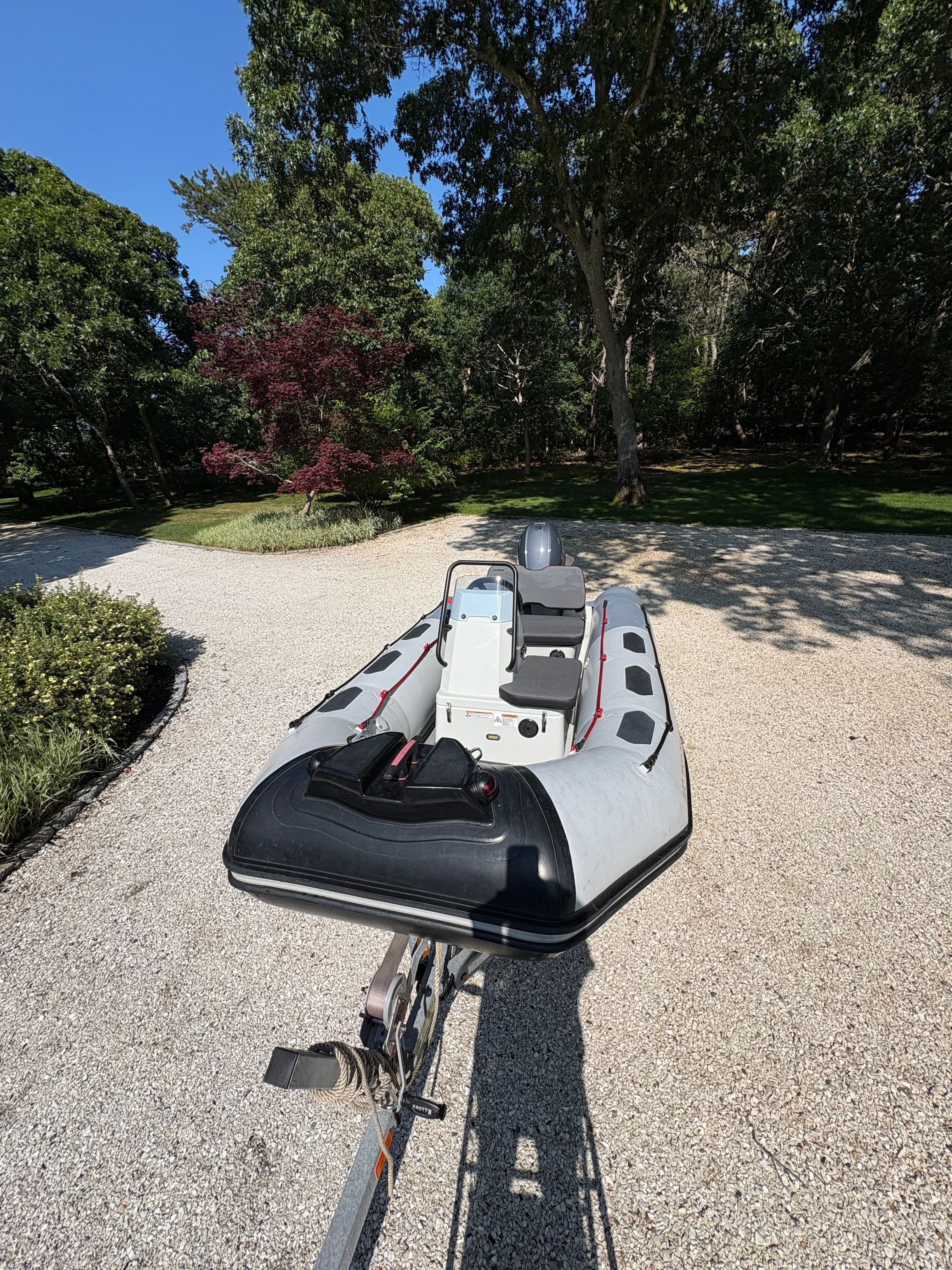 A Zodiac Open 3.4 inflatable boat on a trailer, surrounded by trees and a gravel path.