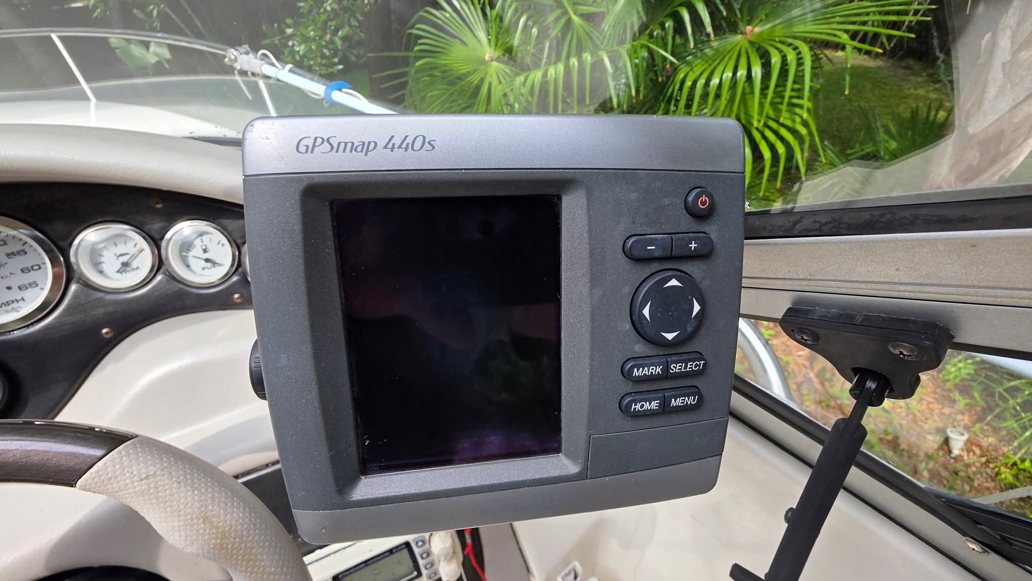 A GPSmap 440s device is mounted on a boat, surrounded by green plants.
