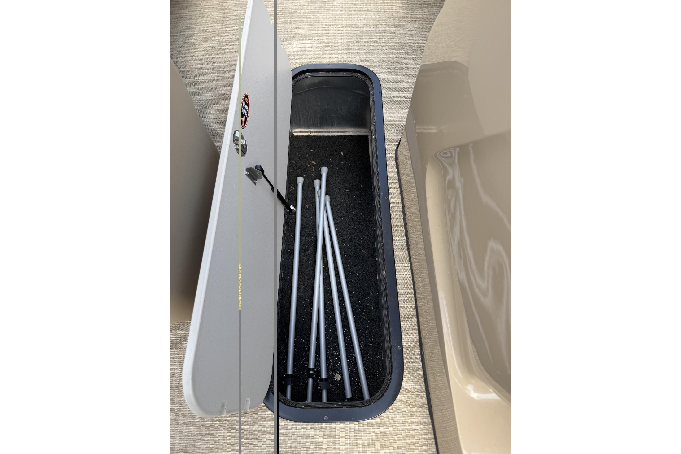 Open storage compartment on 2022 Harris Solstice 230 CWDH boat, containing metal poles.