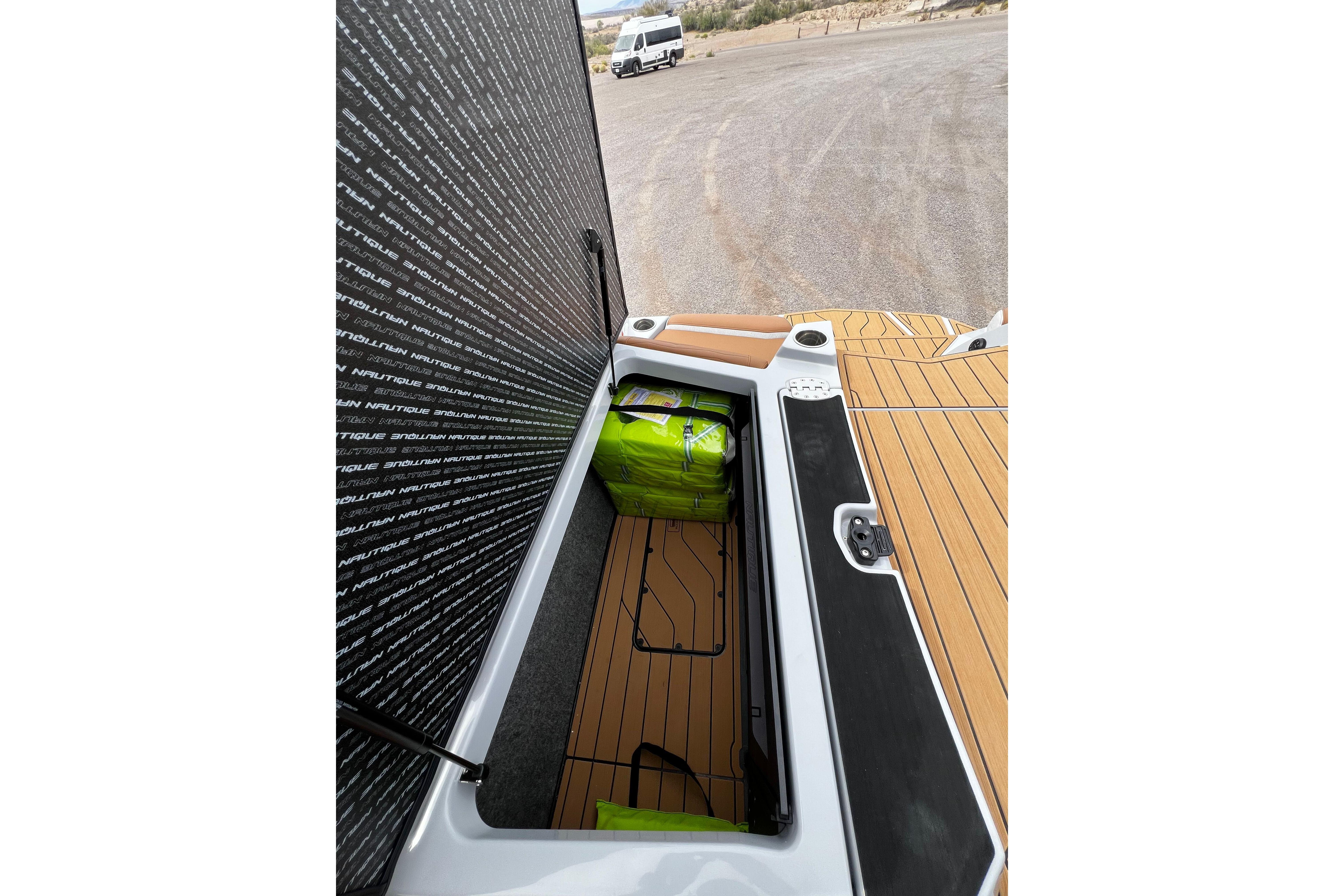 2026 Nautique Super Air Nautique G25 storage compartment with green bags on teak deck.
