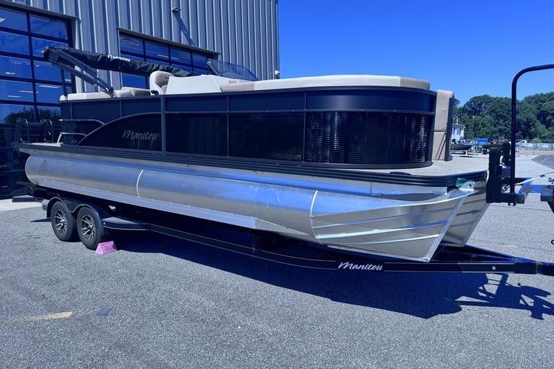 2027 Manitou Aurora 23 RF SHP pontoon boat on trailer, parked outdoors.