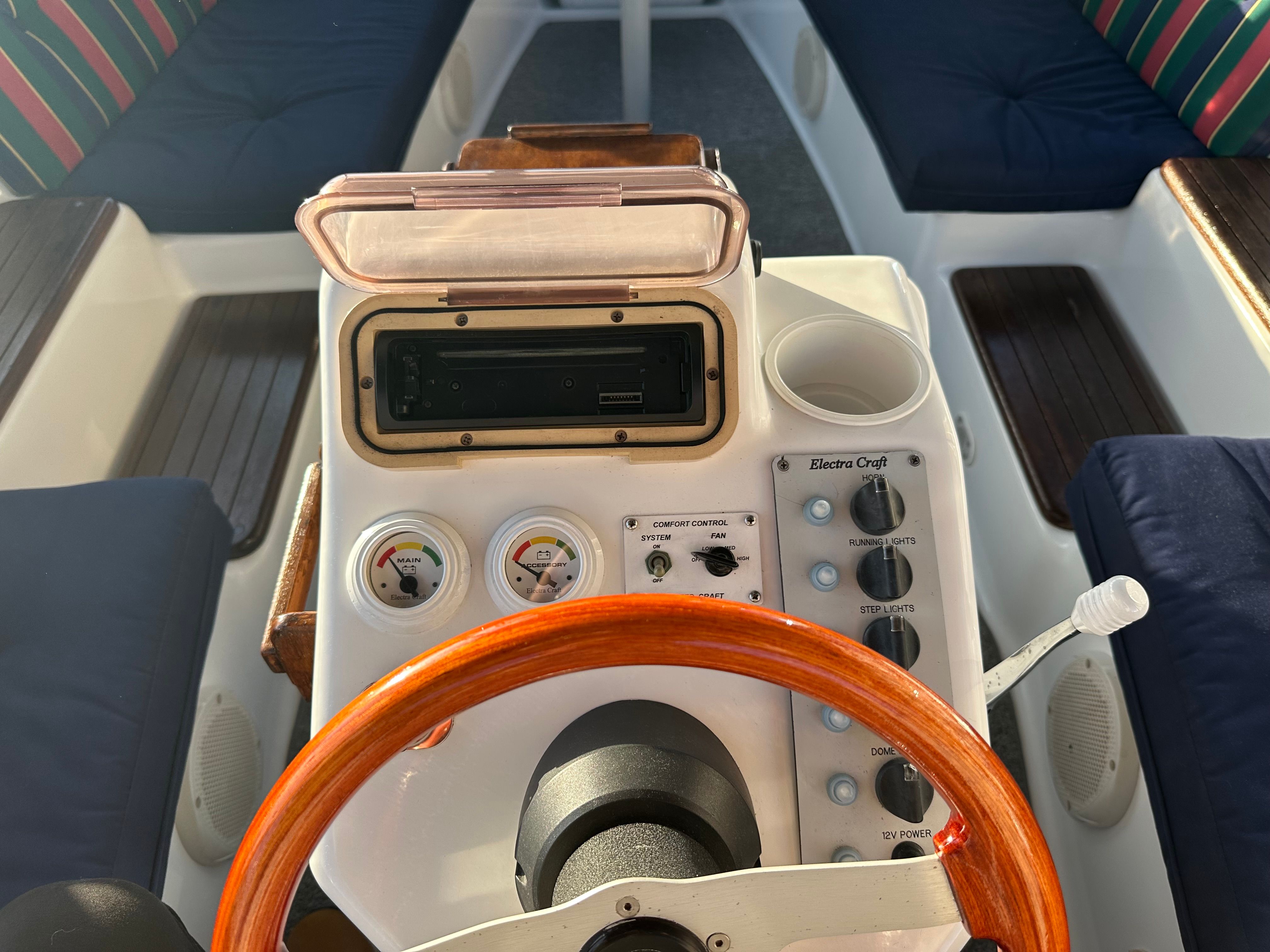 The image shows a boat's helm with a wooden steering wheel and various instruments.