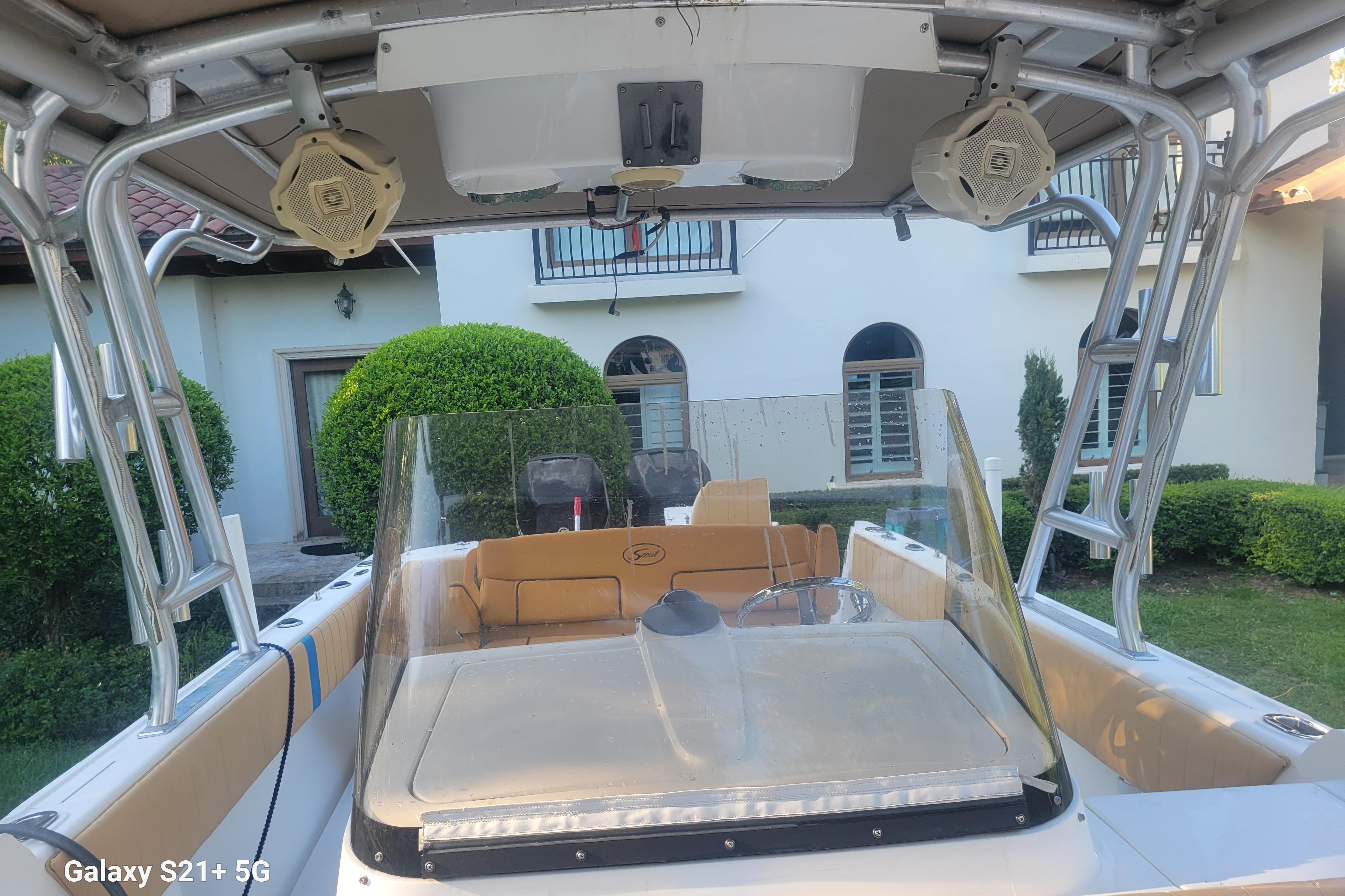 2005 Intrepid 323 Cuddy boat with seating, speakers, and windshield, parked near a house.