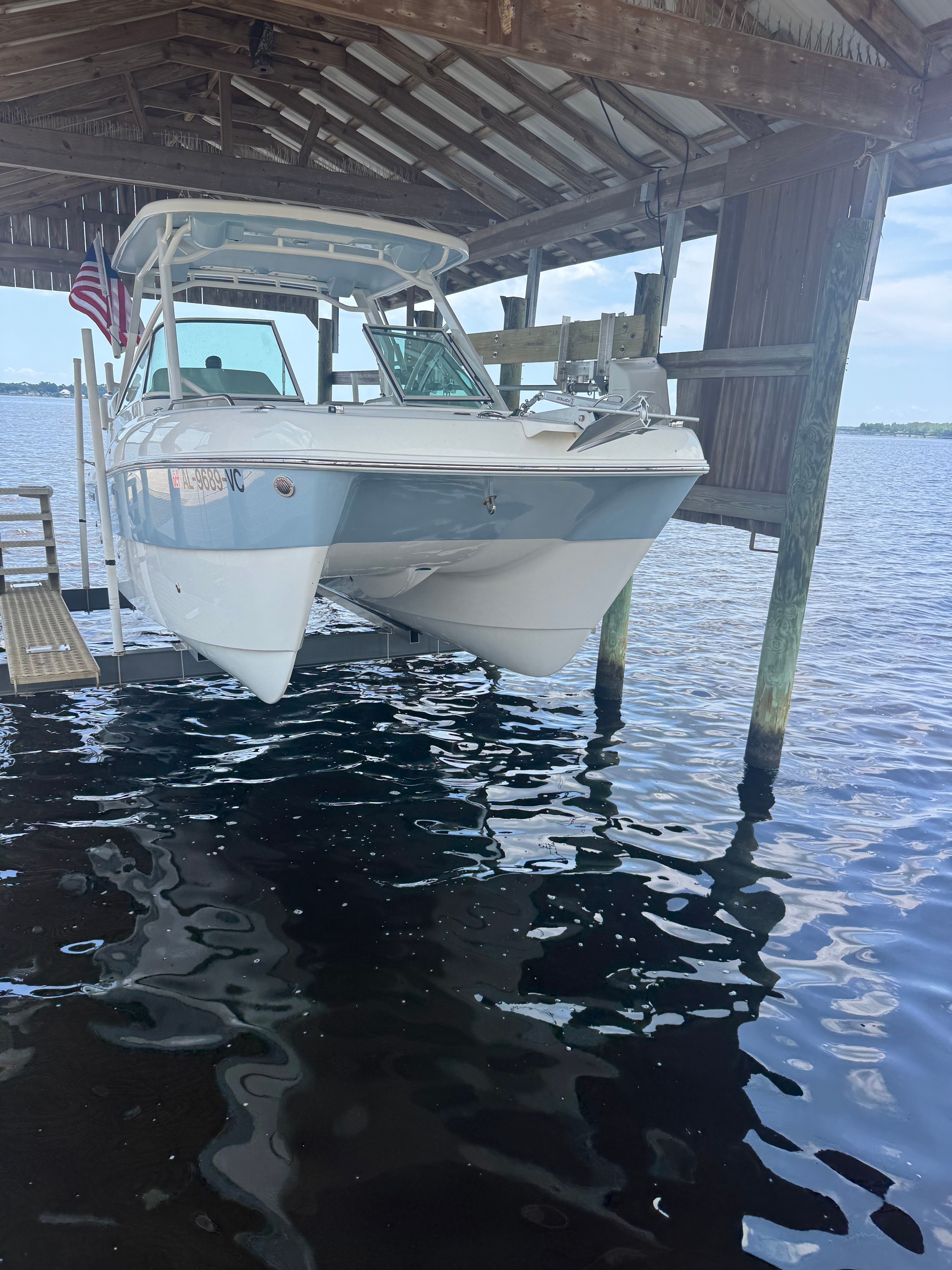 A 2025 World Cat 230 DC boat is stored in a covered boathouse above the water.