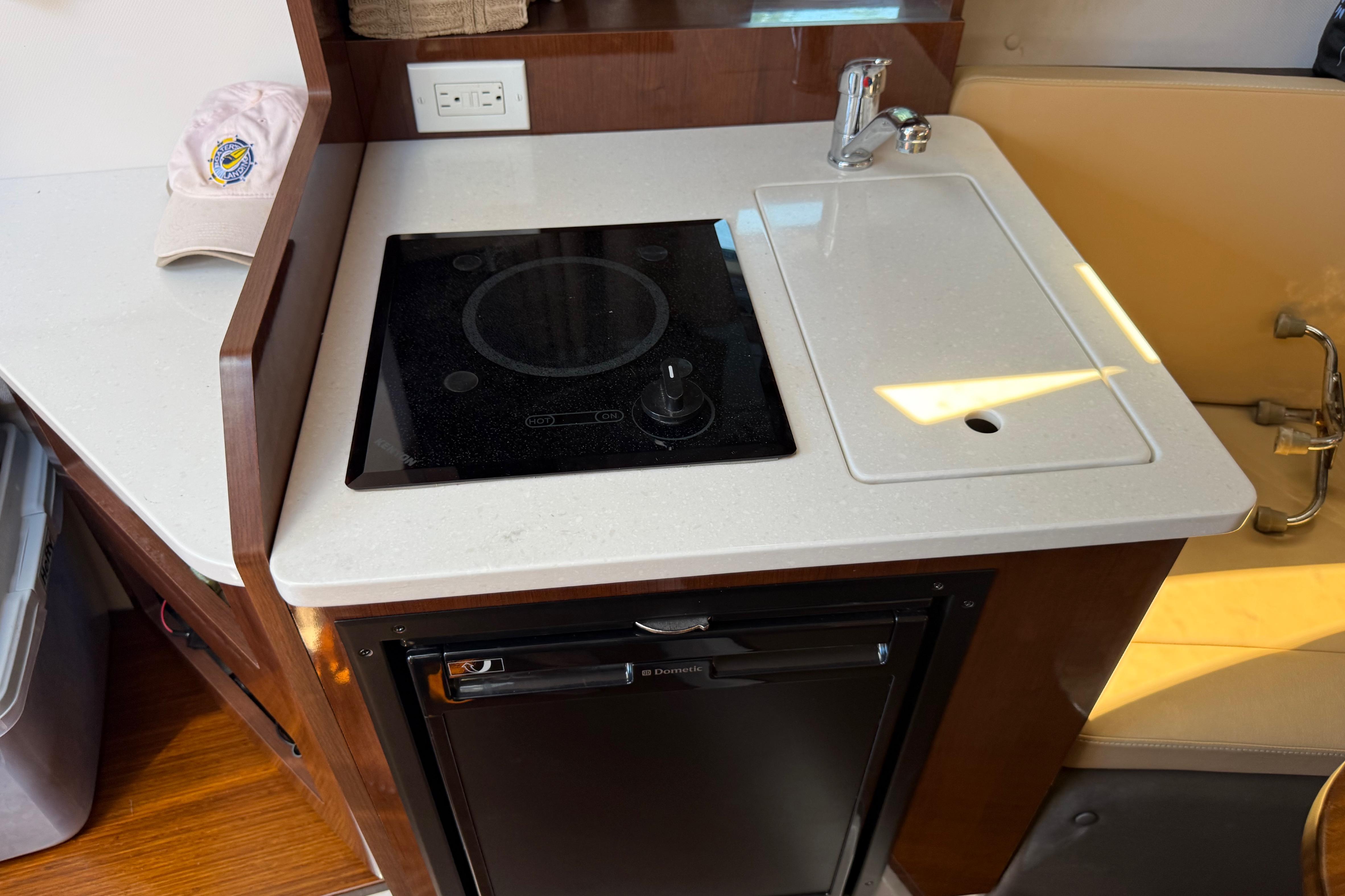 Compact kitchen area in a 2017 Four Winns V275 boat with stove and sink.