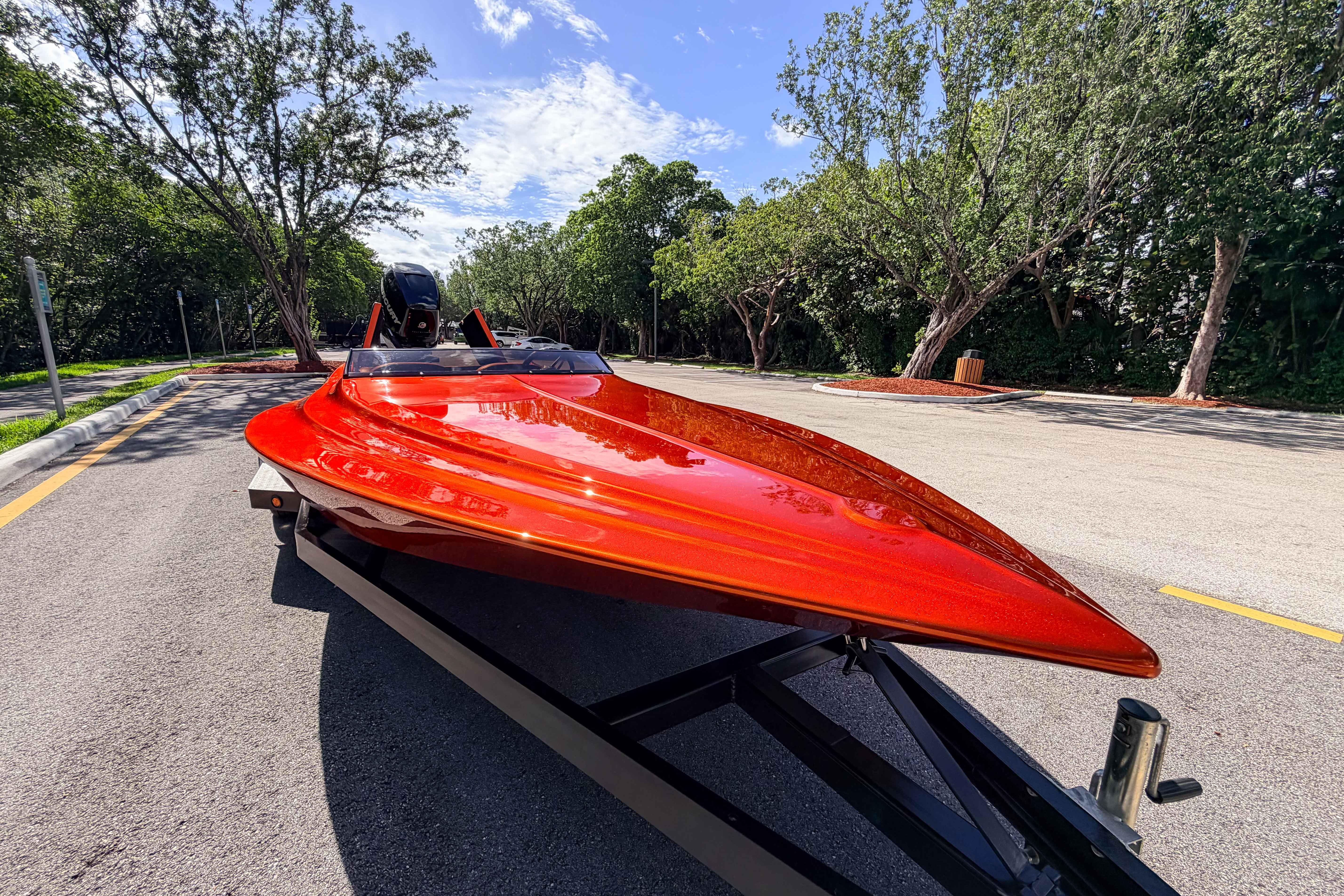 1984 Sleekcraft Aristocrat 20 boat with vibrant red finish on a trailer, surrounded by trees.