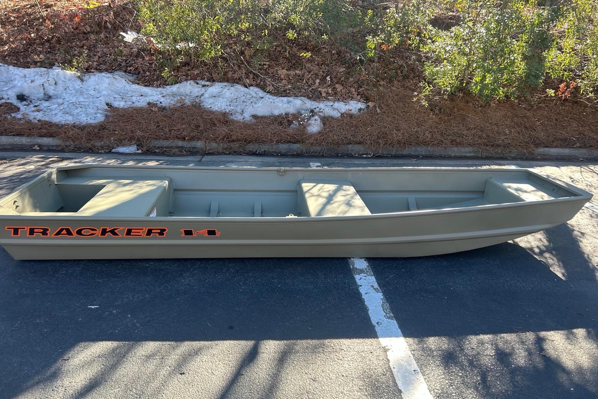 2026 Tracker Grizzly 14 Jon boat parked on asphalt, surrounded by greenery and snow.