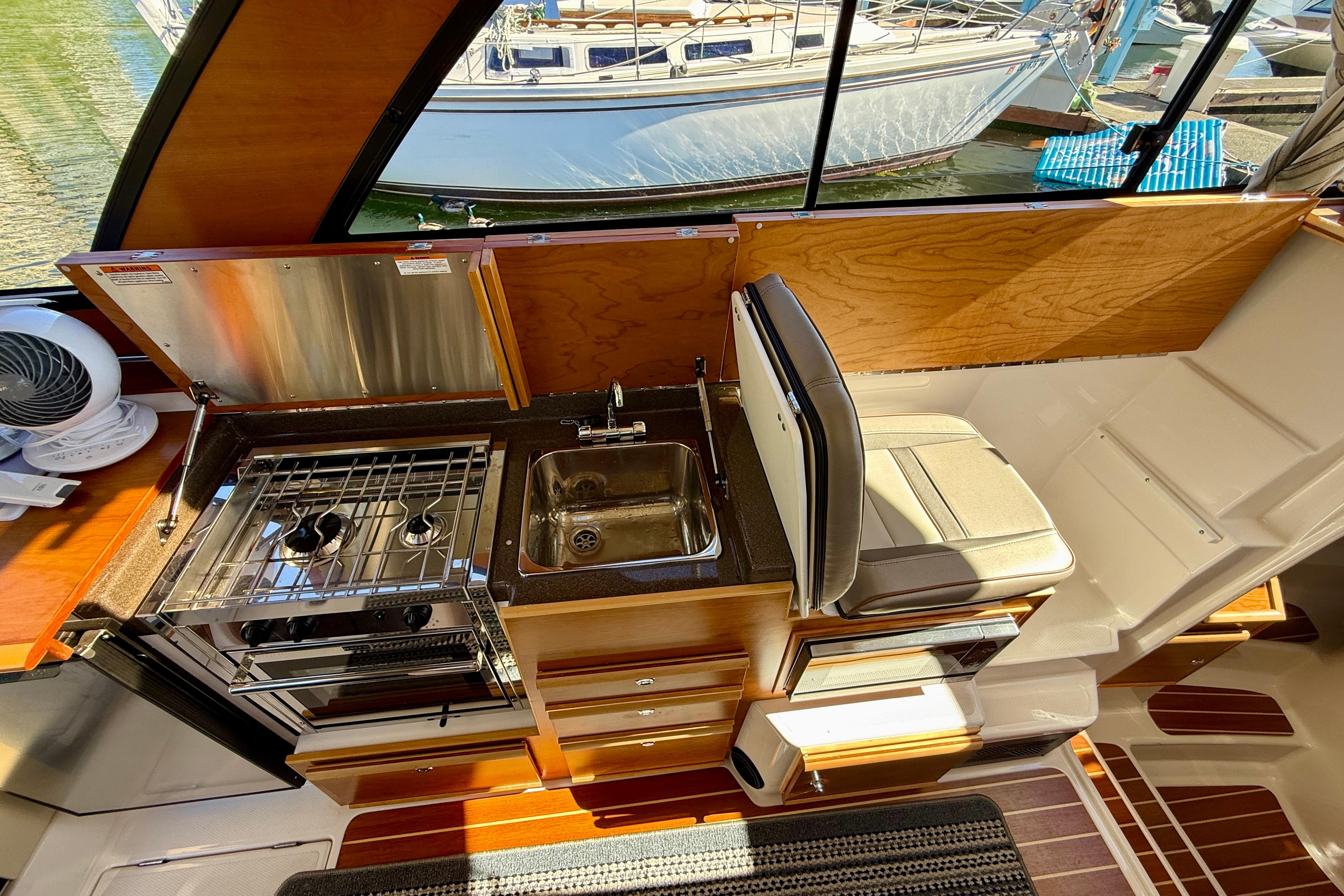 2023 Cutwater C-30 Sedan interior kitchen with stove, sink, and seating.