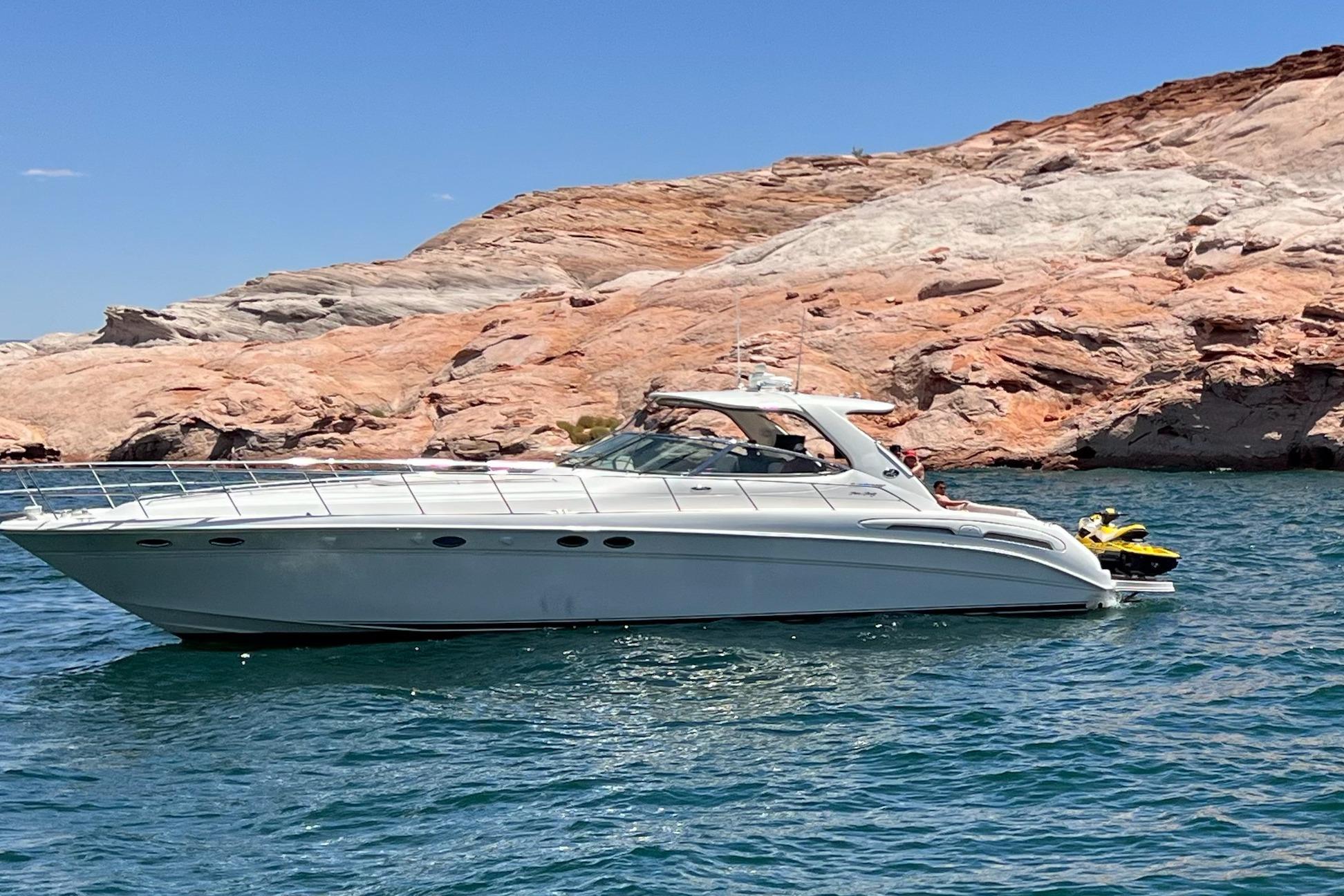 Sea Ray Sundancer 540 yacht cruising near rocky shoreline, 2000 model.