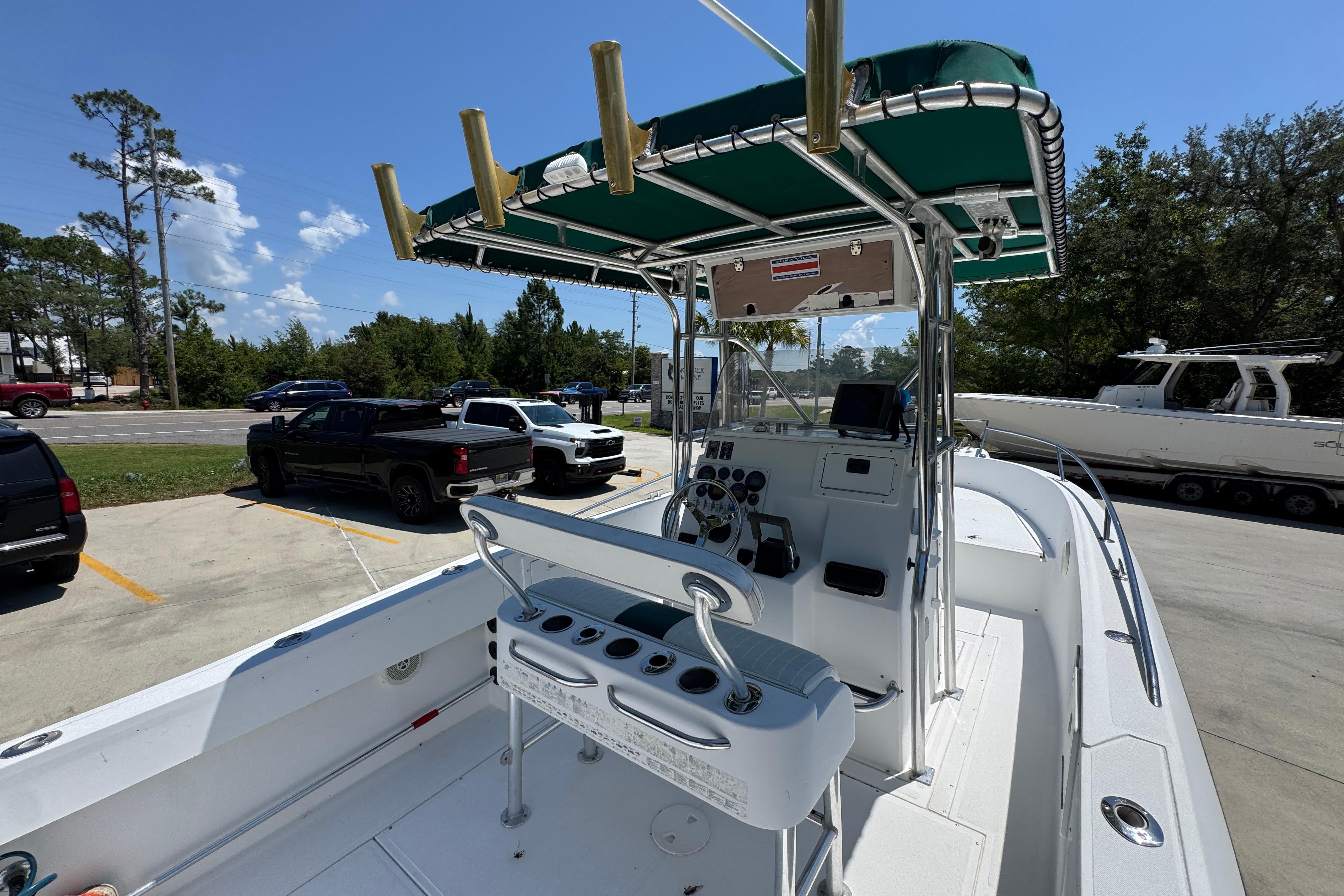 2000 Stamas 250 Tarpon boat with green canopy, parked in a lot under a clear blue sky.