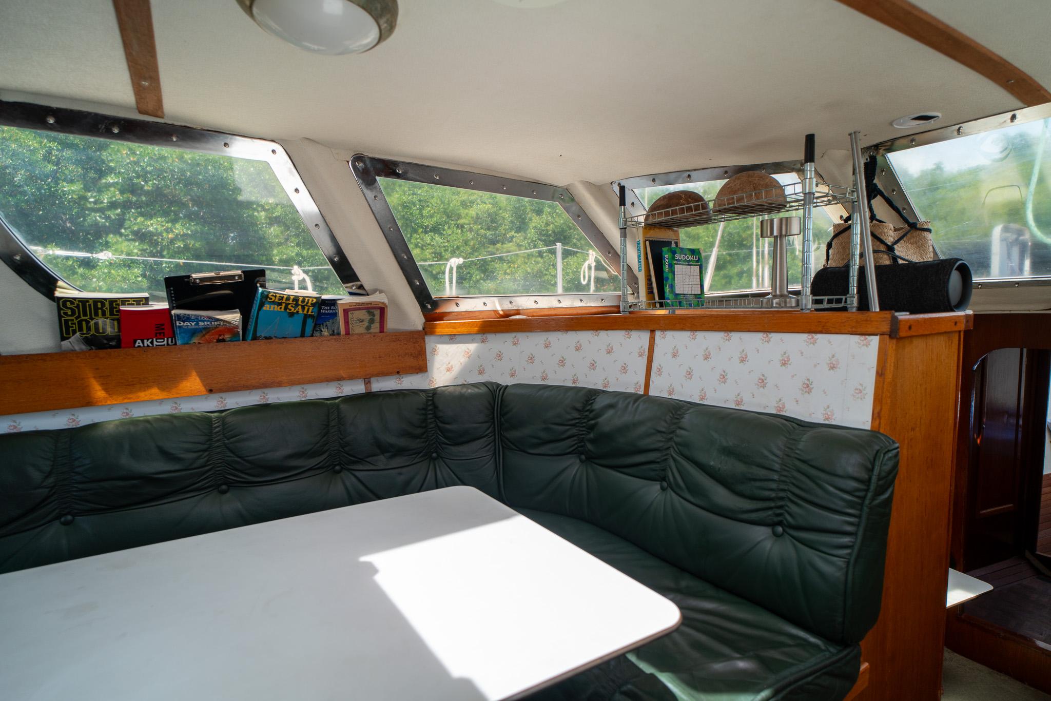Cozy boat interior with green seating, books, and a white table, Custom model 49, 1998.