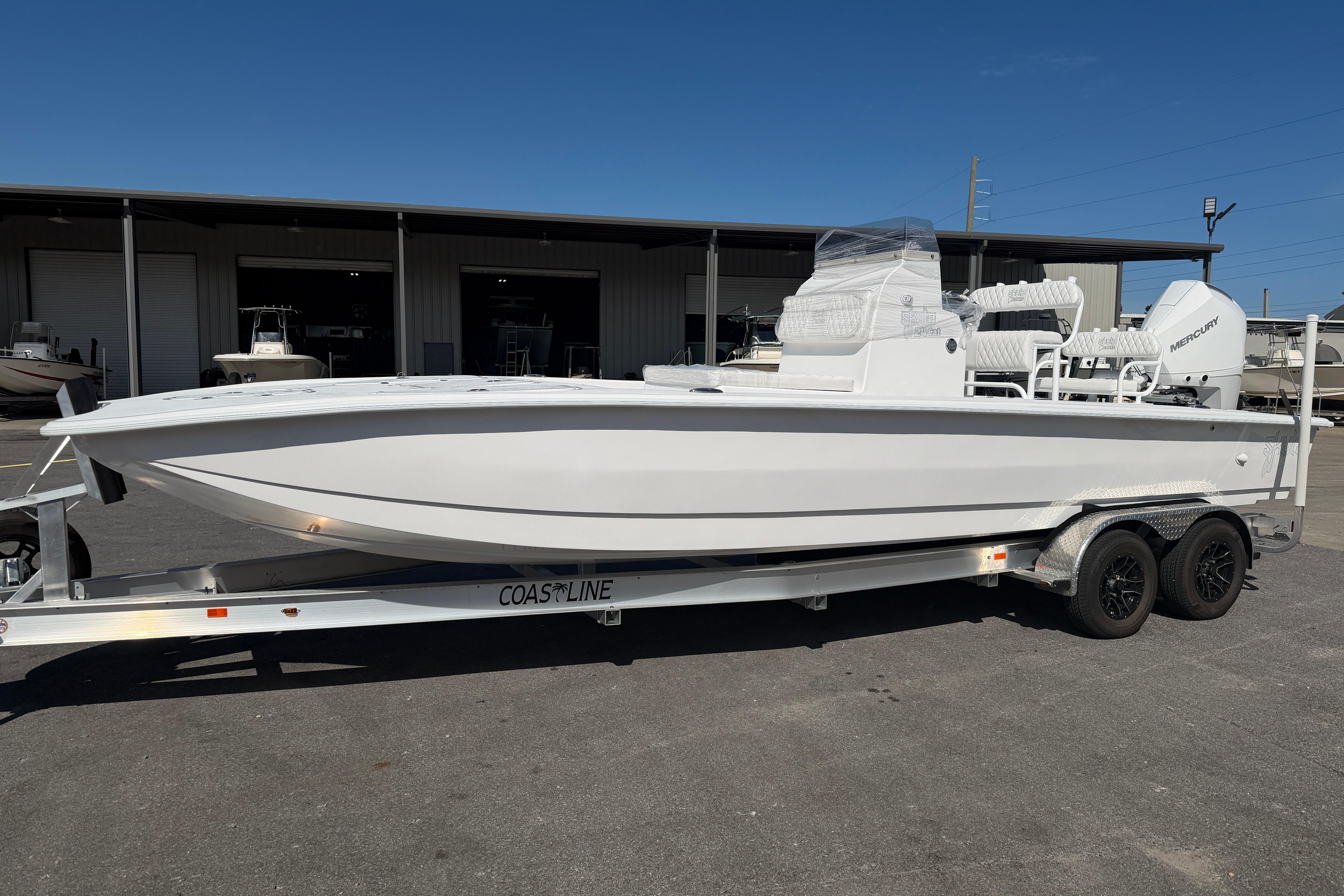 2026 Skuta 24 Cat boat on trailer, parked outdoors under clear blue sky.