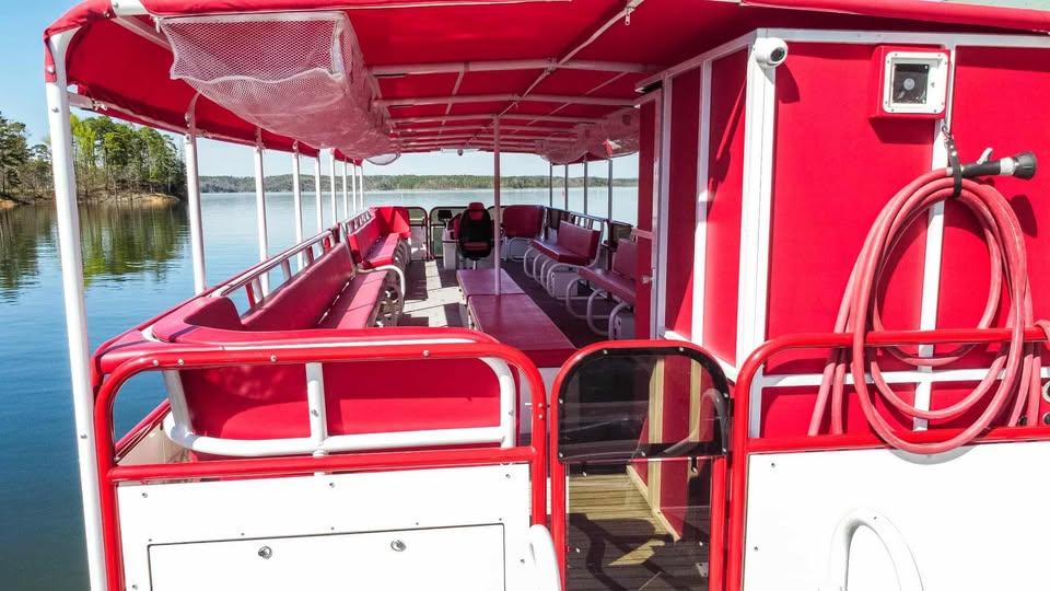 2024 Aloha Pontoon 50' Water Taxi with red seating and canopy on a calm lake.