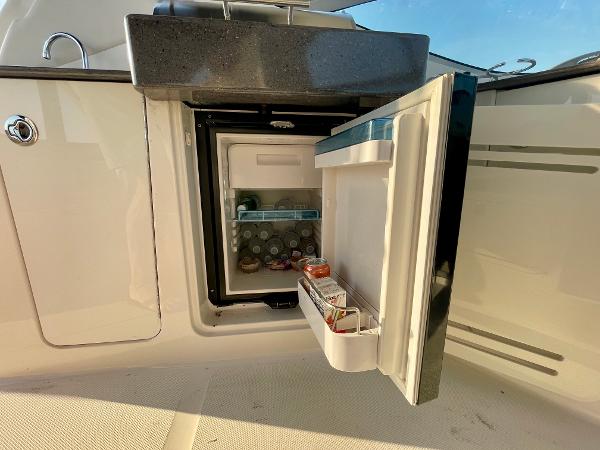 Open mini fridge on 2014 Sea Ray 330 Sundancer boat, stocked with beverages.