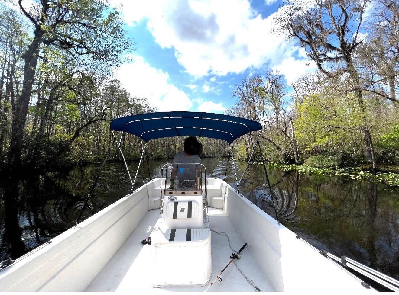 A 2011 Carolina Skiff 258 DLV navigates a wooded river under a blue sky.