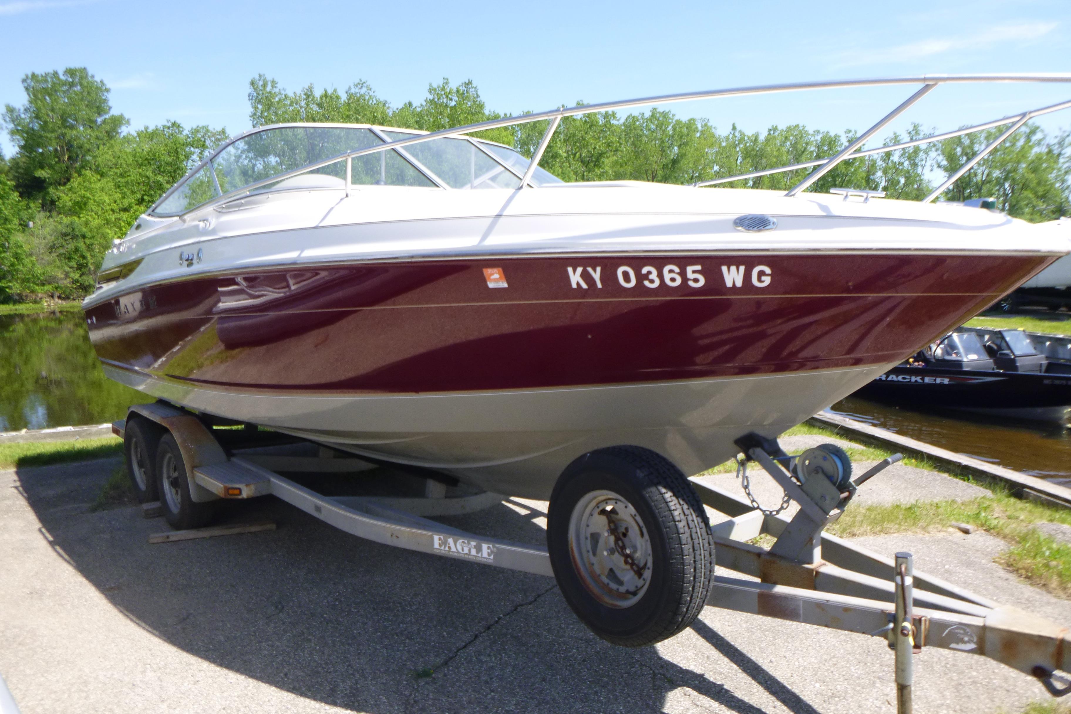 1998 Maxum 2300 SC boat on trailer, parked near a lake with lush greenery.