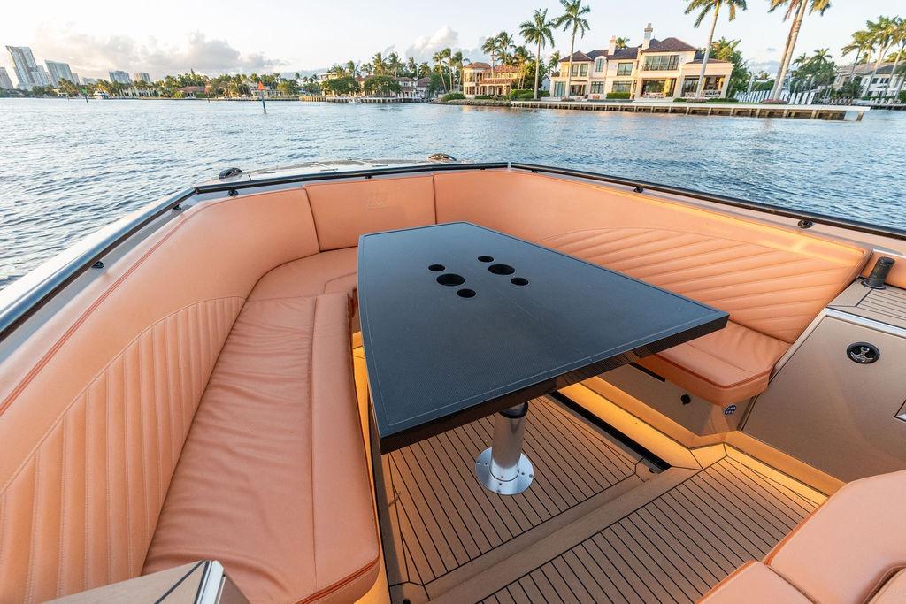 Luxurious 2023 DeKoning 43 yacht interior with elegant seating and table, overlooking waterfront homes.