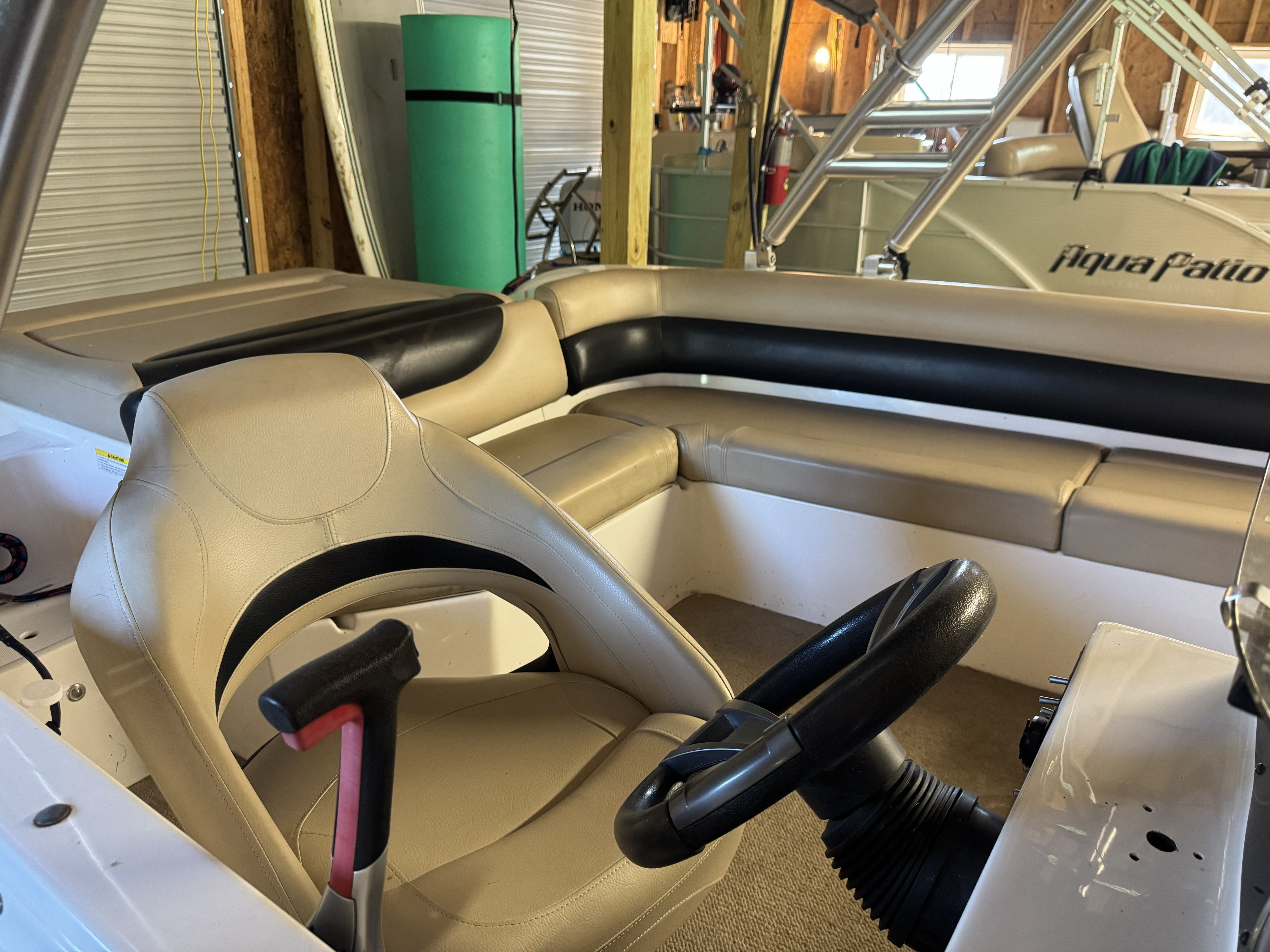 Interior view of a boat with beige and black seating, steering wheel, and upholstery.