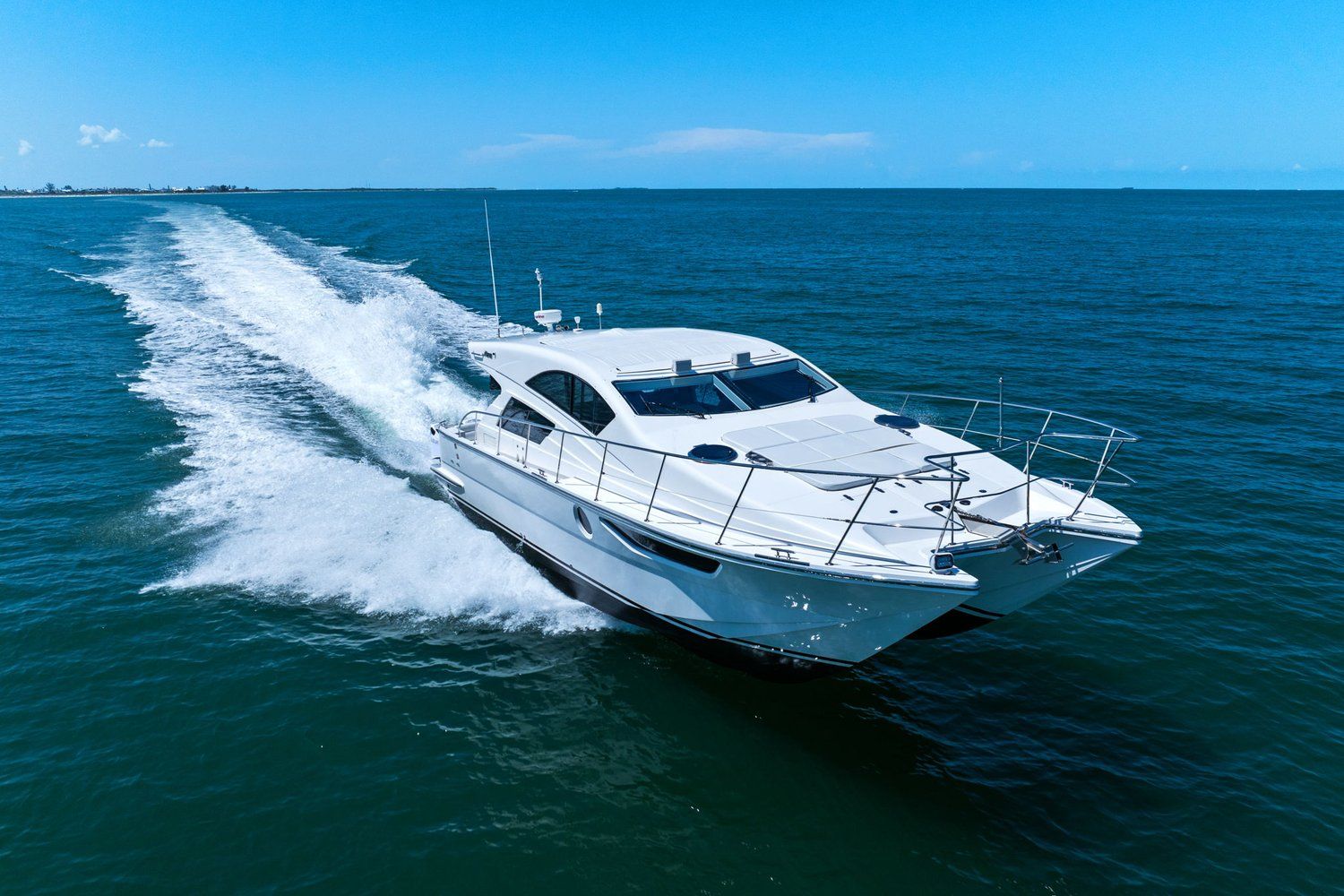 A white catamaran speeds across the blue sea, leaving a trail of spray.