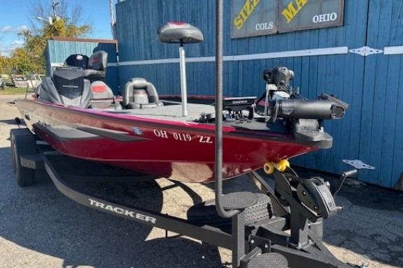 2025 Tracker Savage 215 boat on trailer, parked outdoors near blue building.