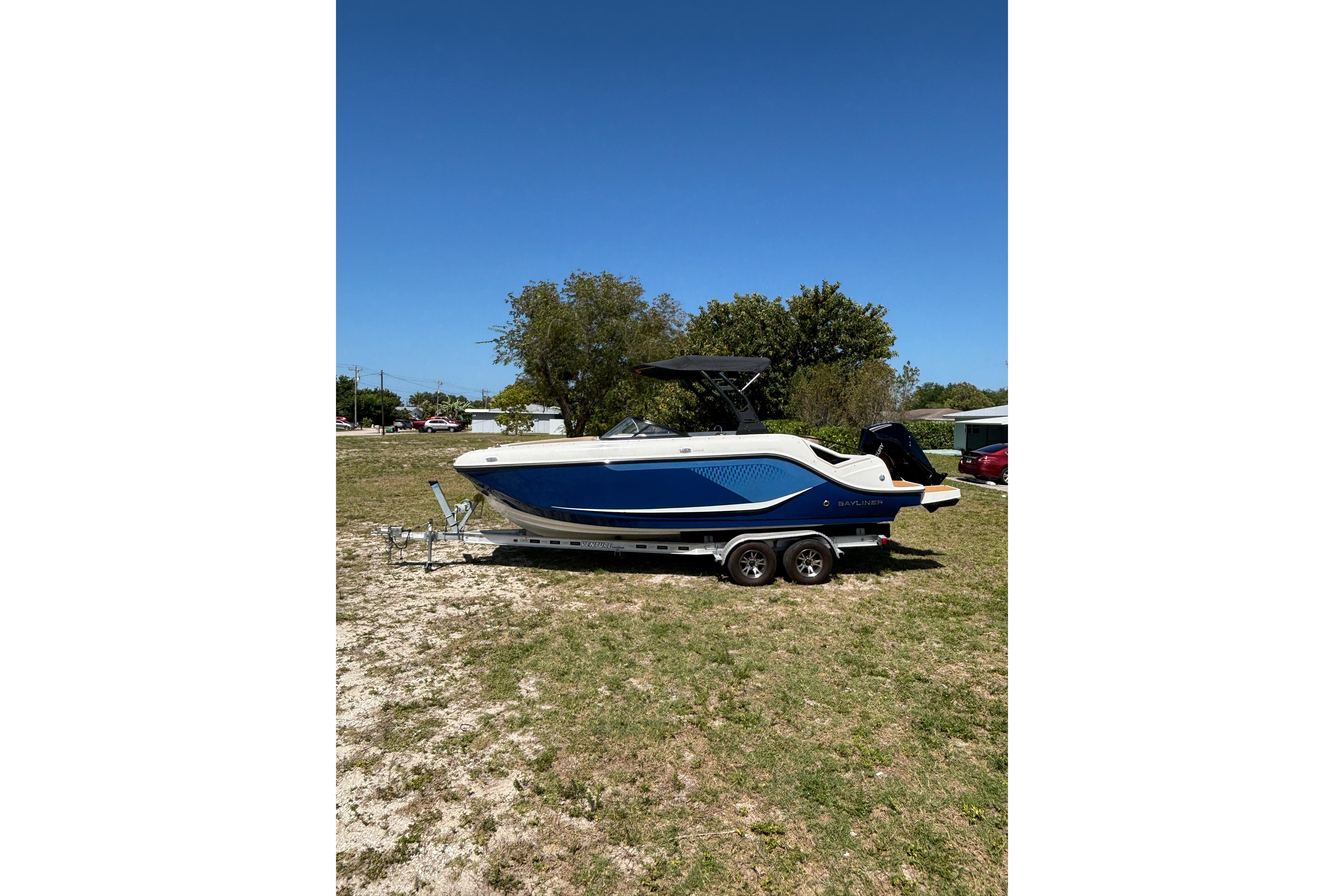 2026 Bayliner D22 boat on trailer, parked on grassy area under clear blue sky.