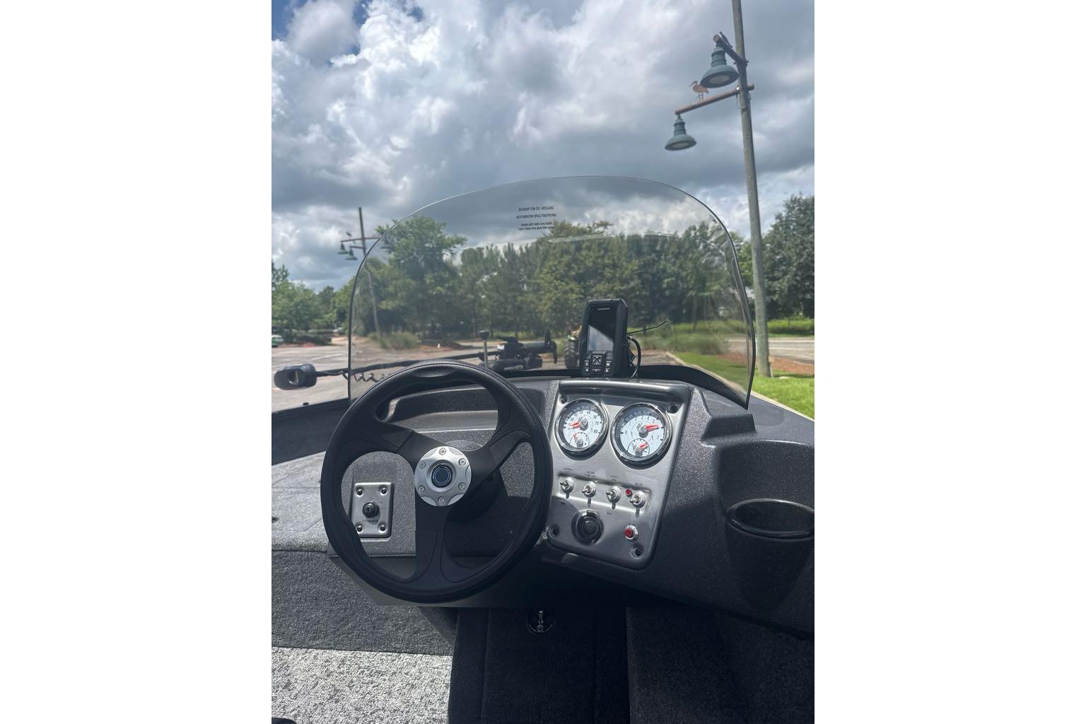 2026 Tracker Pro Guide V-16 SC boat dashboard with steering wheel and gauges under cloudy sky.