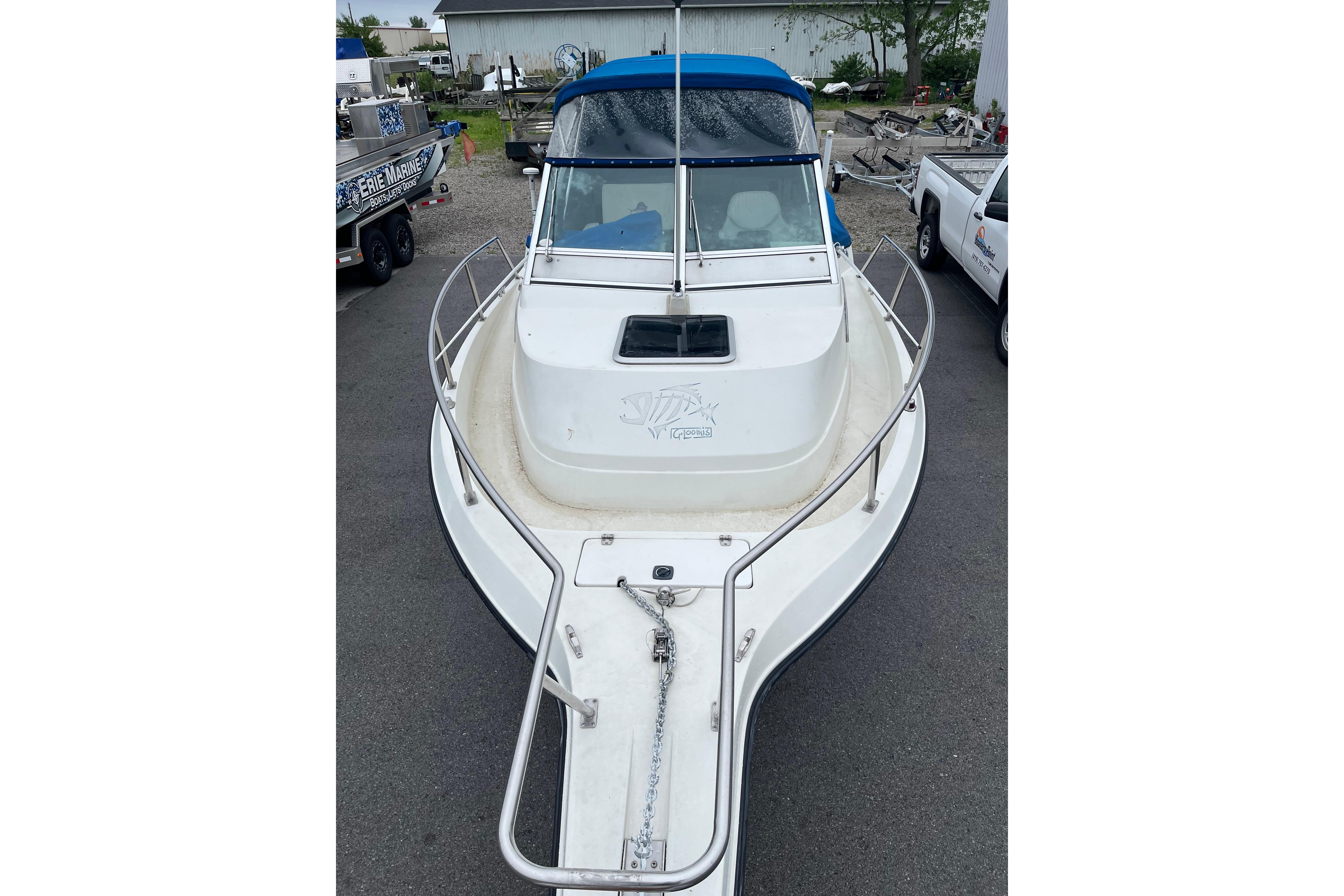 1995 Celebrity 2500 Fish Hawk boat with blue canopy, parked on pavement.